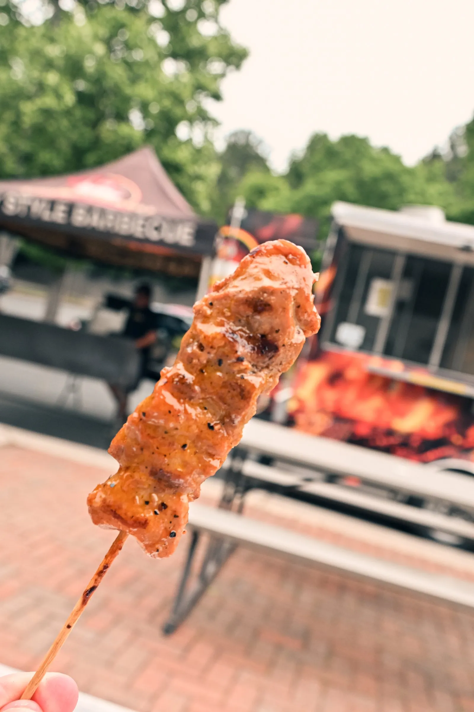 A barbecue skewer held up in front of the Pinoy Style Barbecue tent