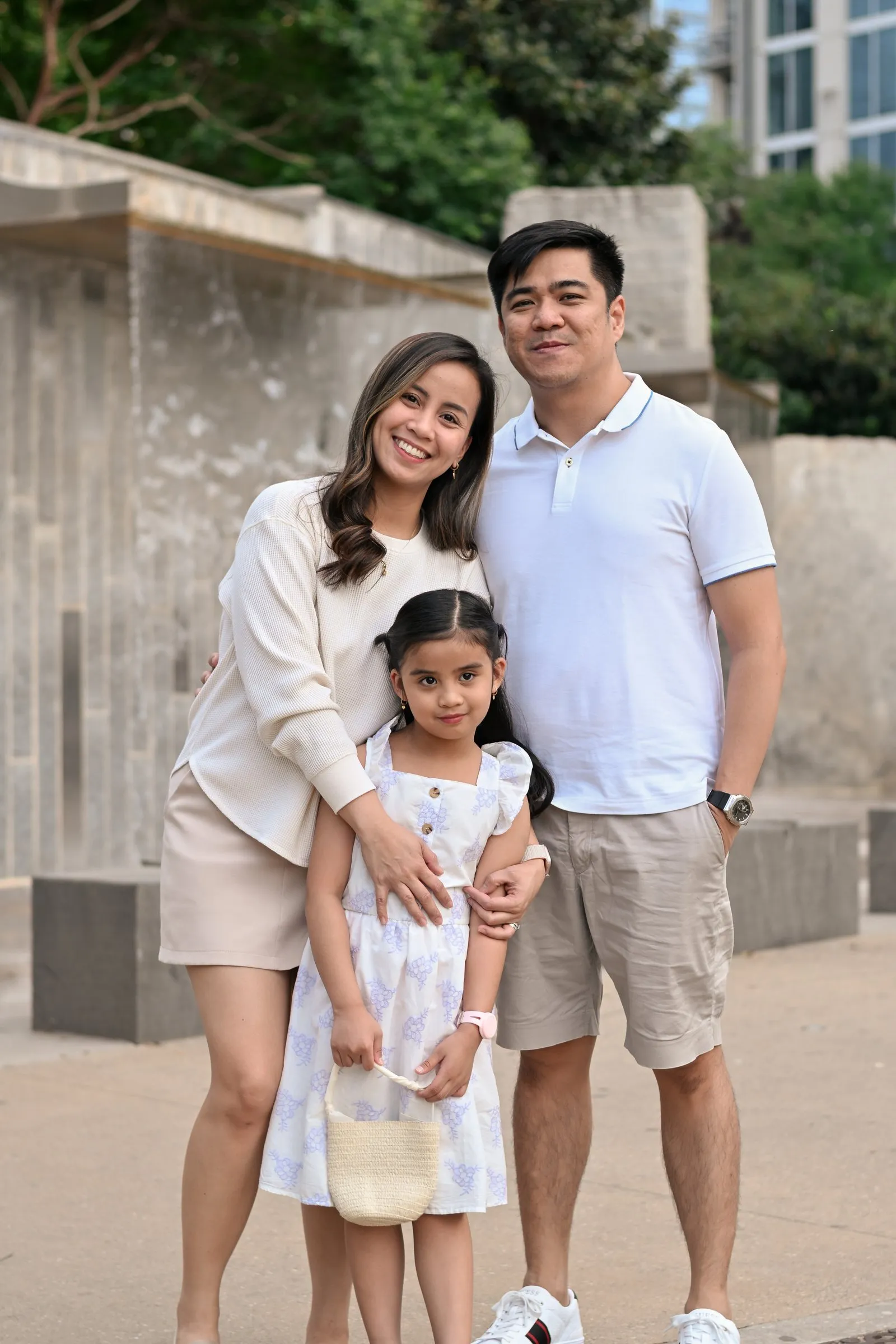 The family standing close together in front of the park's stone wall, Uptown towers behind the trees