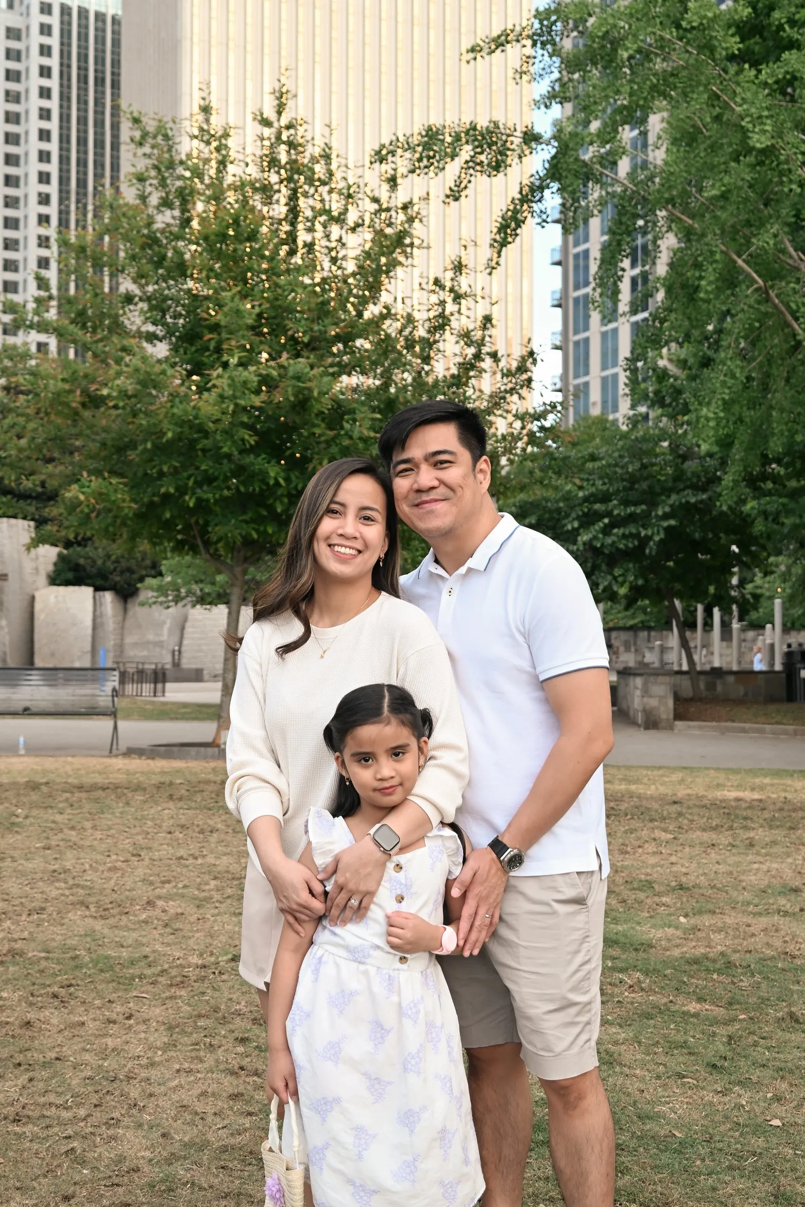Jessica and Jet hugging their daughter on the lawn among the trees and towers