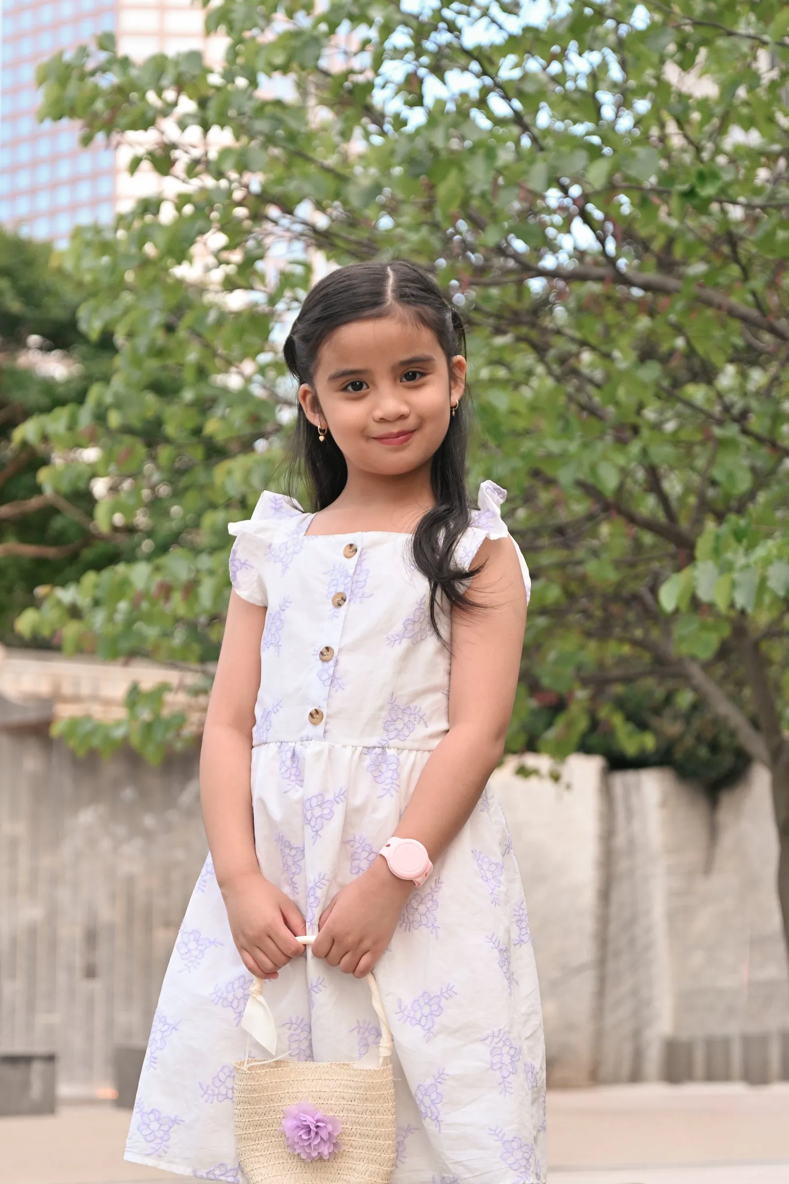 Their daughter in a floral sundress holding a woven purse, a tower rising behind the trees