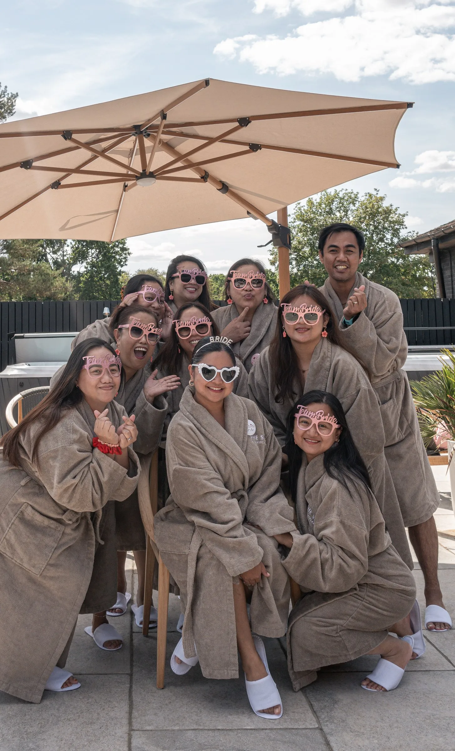 Mathelle and her bridesmaids in matching robes and heart sunglasses posing under a patio umbrella
