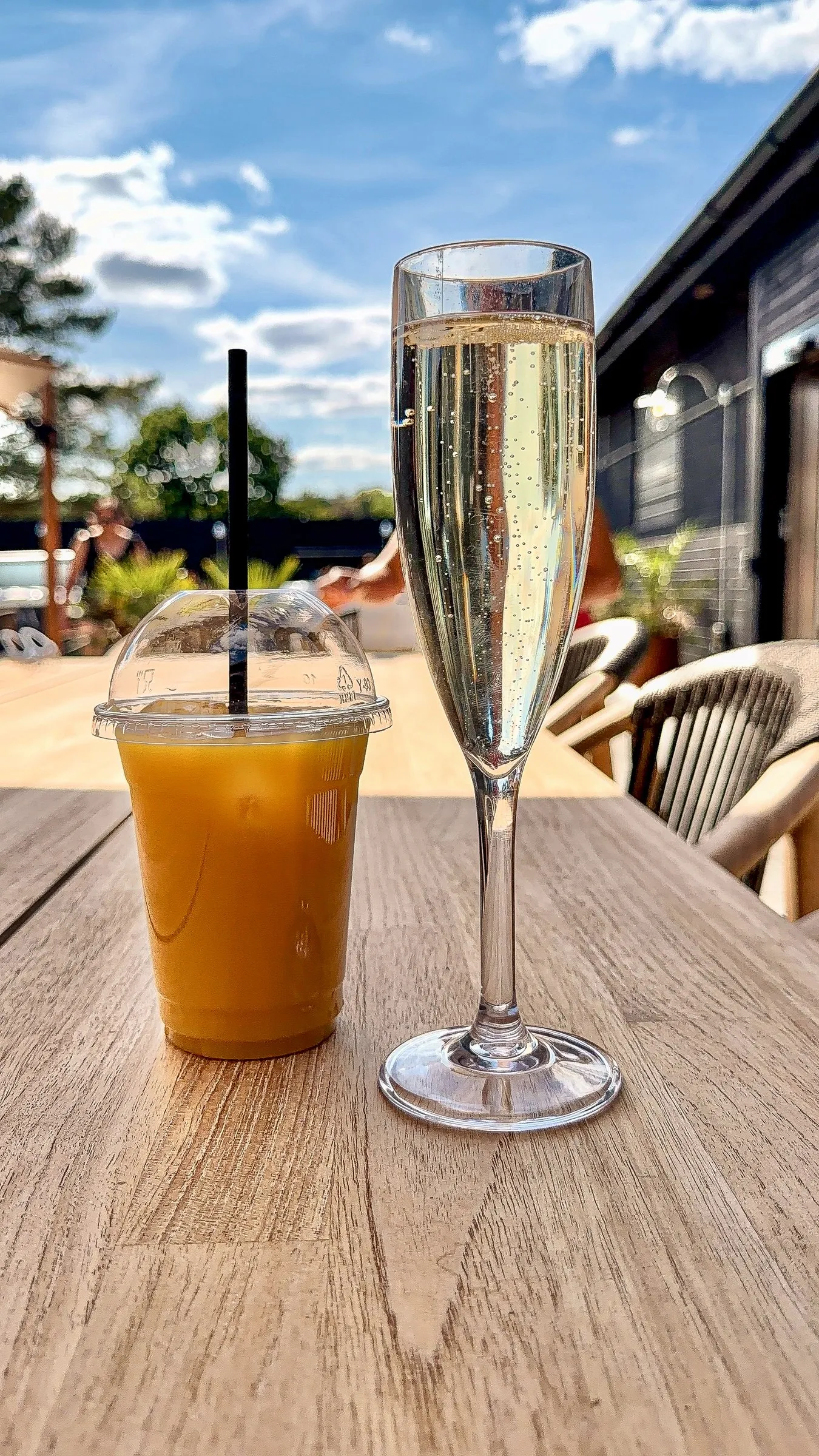 An orange cocktail and a flute of champagne on the patio table under a blue sky