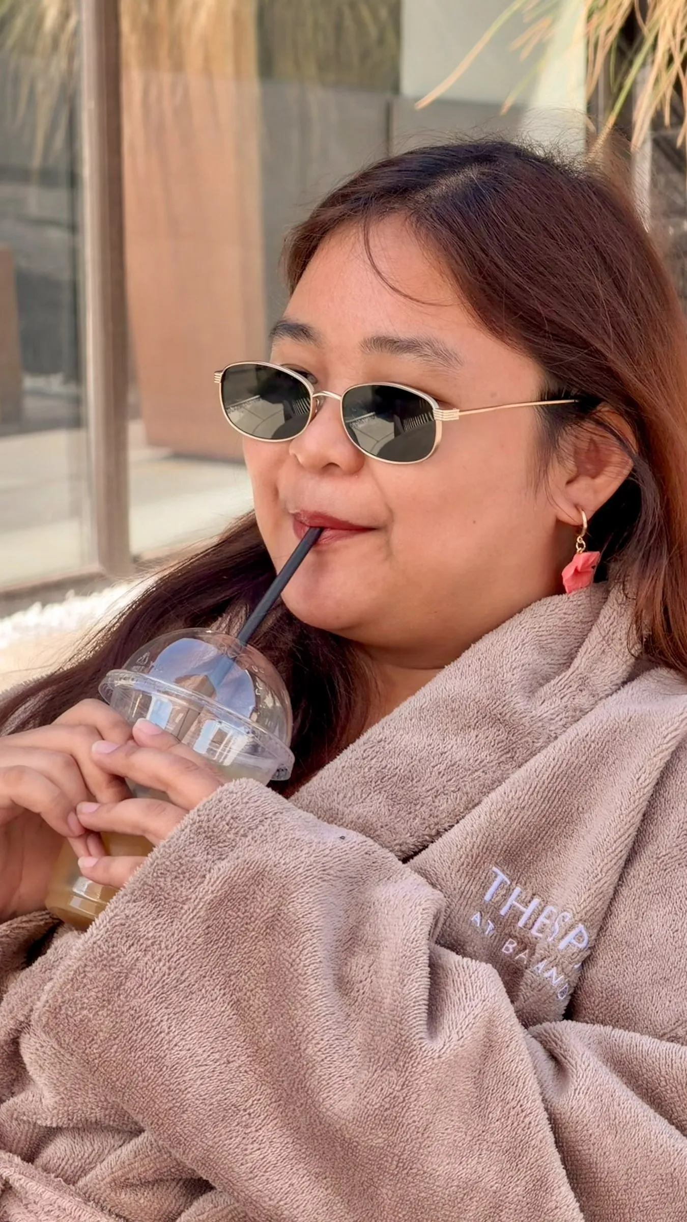 A friend in sunglasses sipping an iced drink in her robe