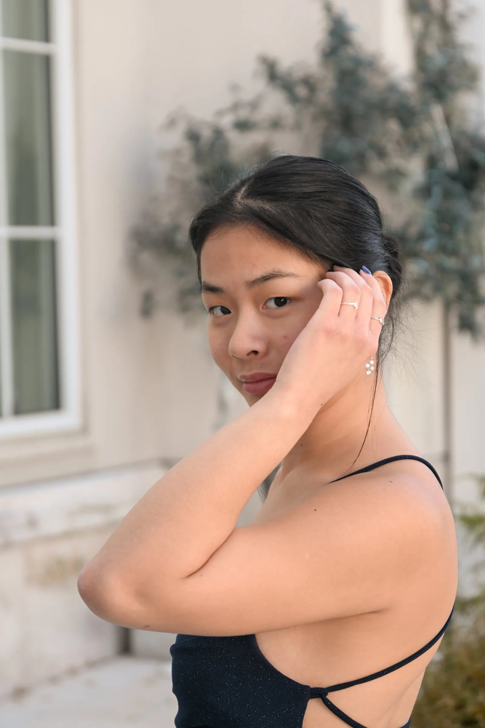 Meilin glancing back over her shoulder in a navy open back dress, hand resting in her hair beside a white window