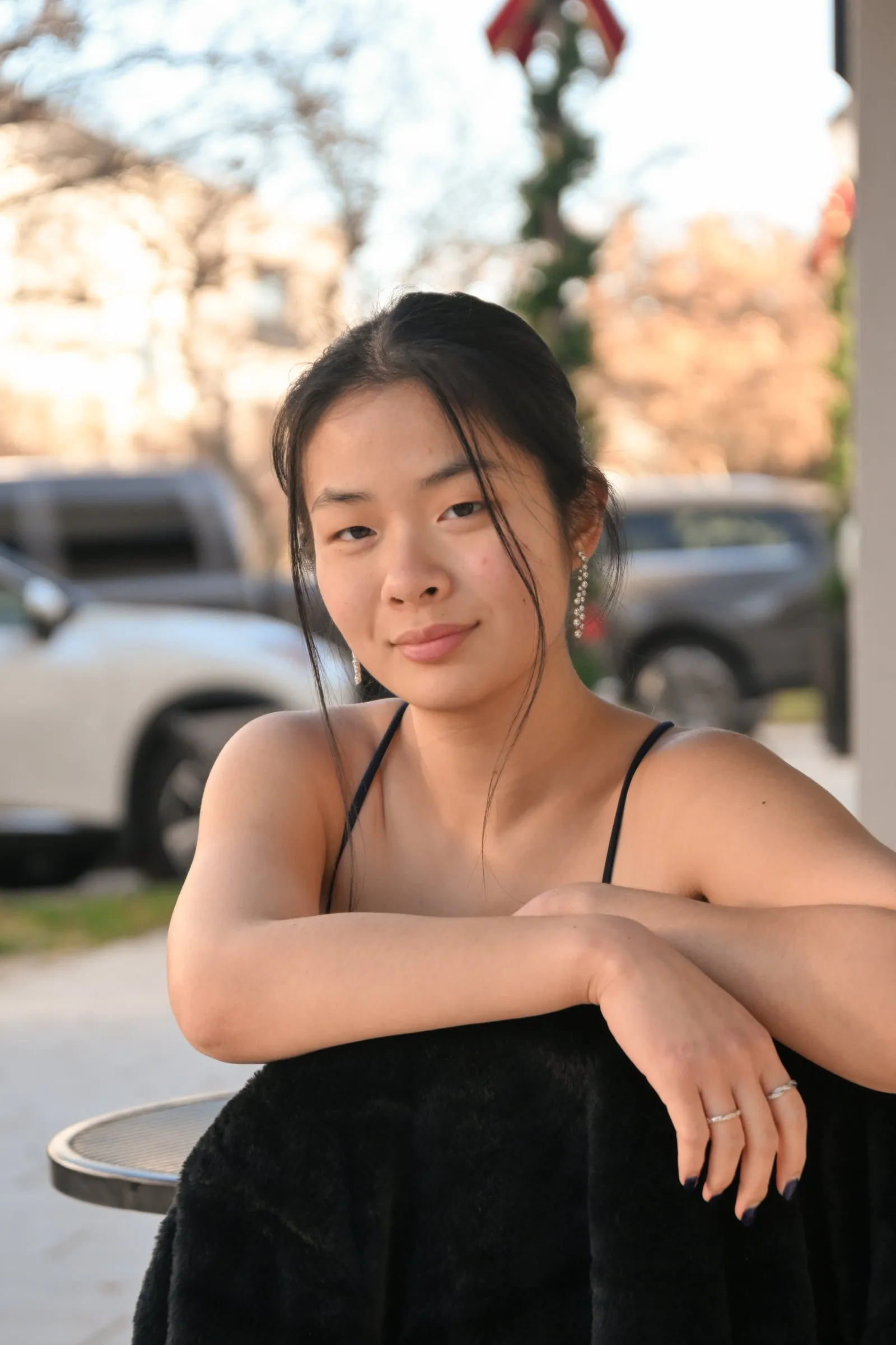 Meilin leaning on a chair draped in a black faux fur wrap, a holiday garland and the street softly blurred behind her