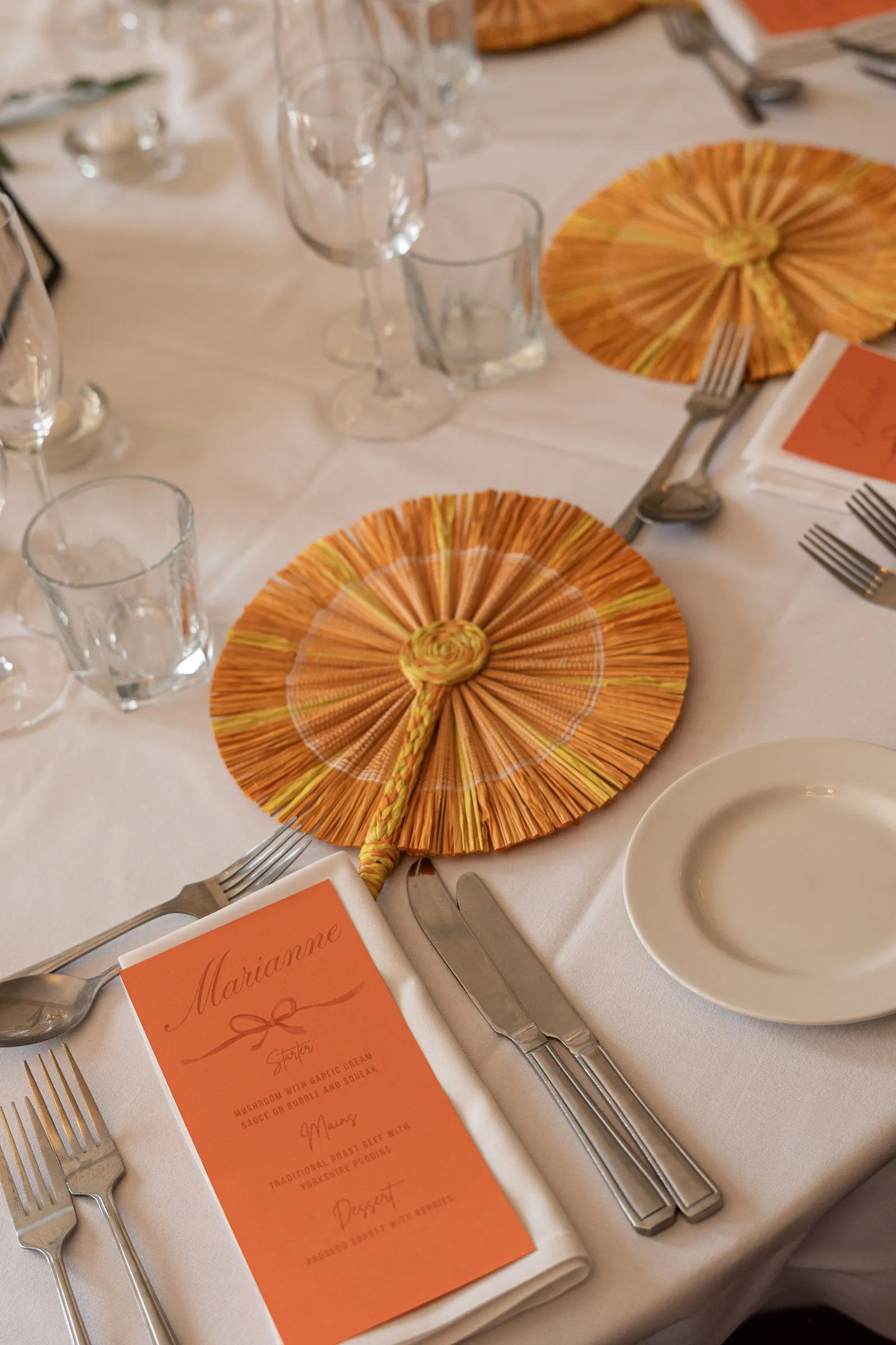 Reception place setting with a gold and peach paper fan, menu card and glassware