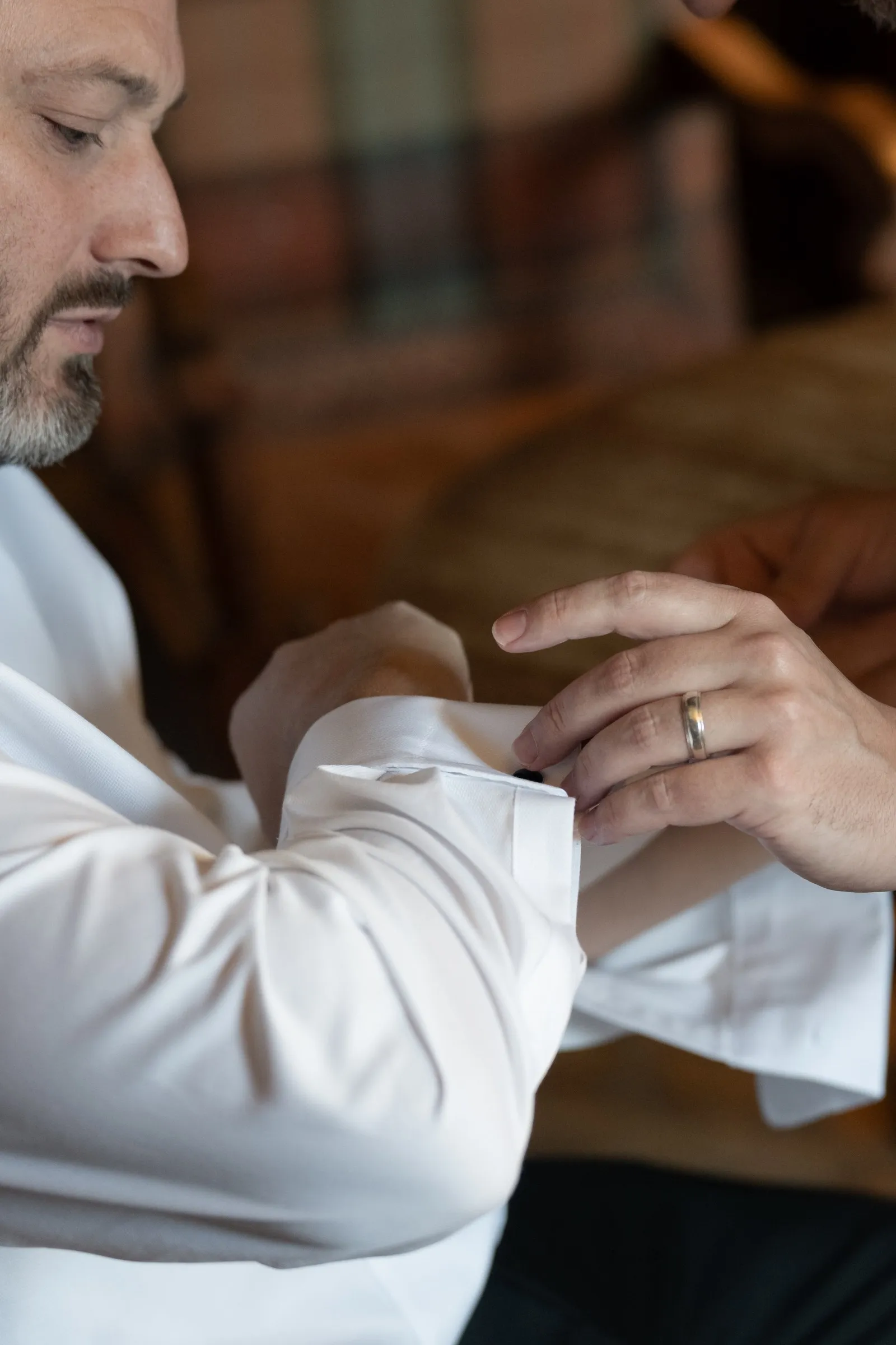 Close-up of Mitch fastening his shirt cuff, wedding band on his finger