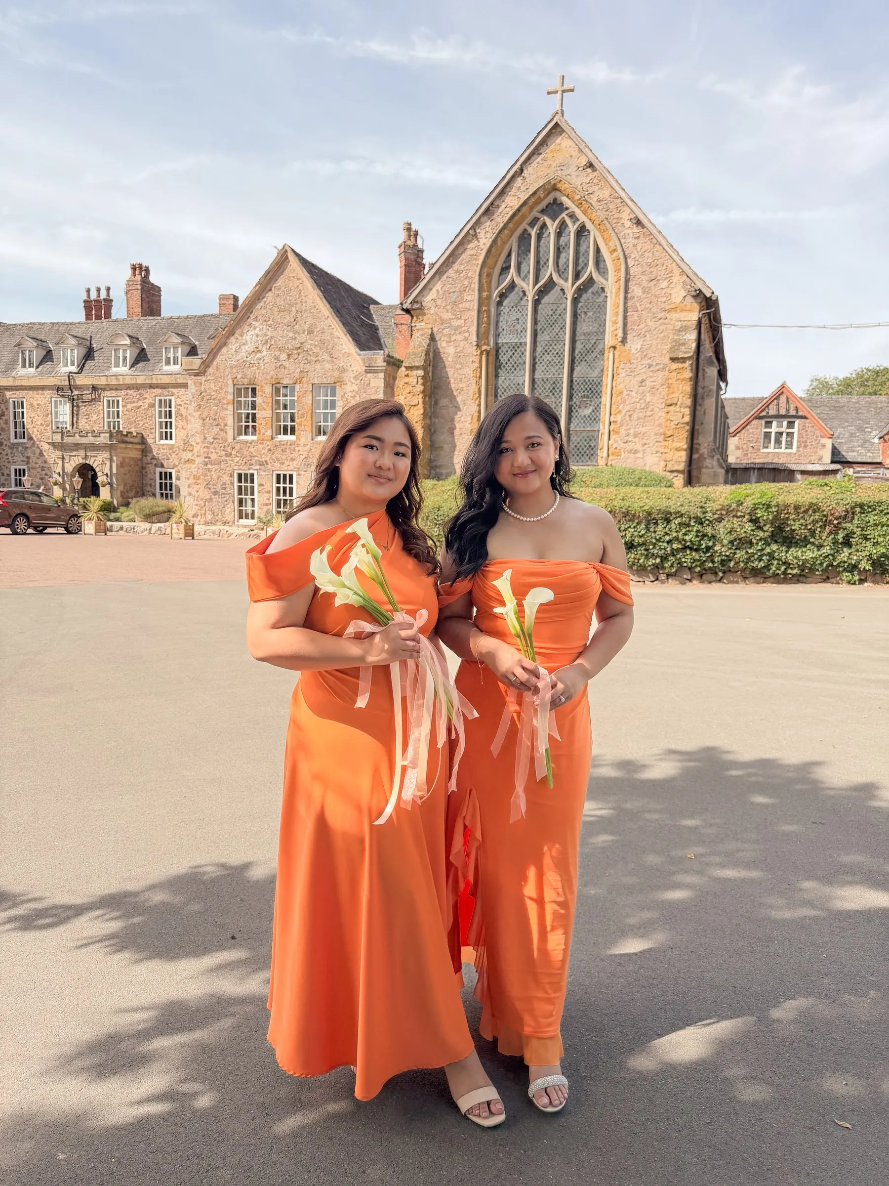 Two bridesmaids in peach dresses holding calla lilies in front of Rothley Court