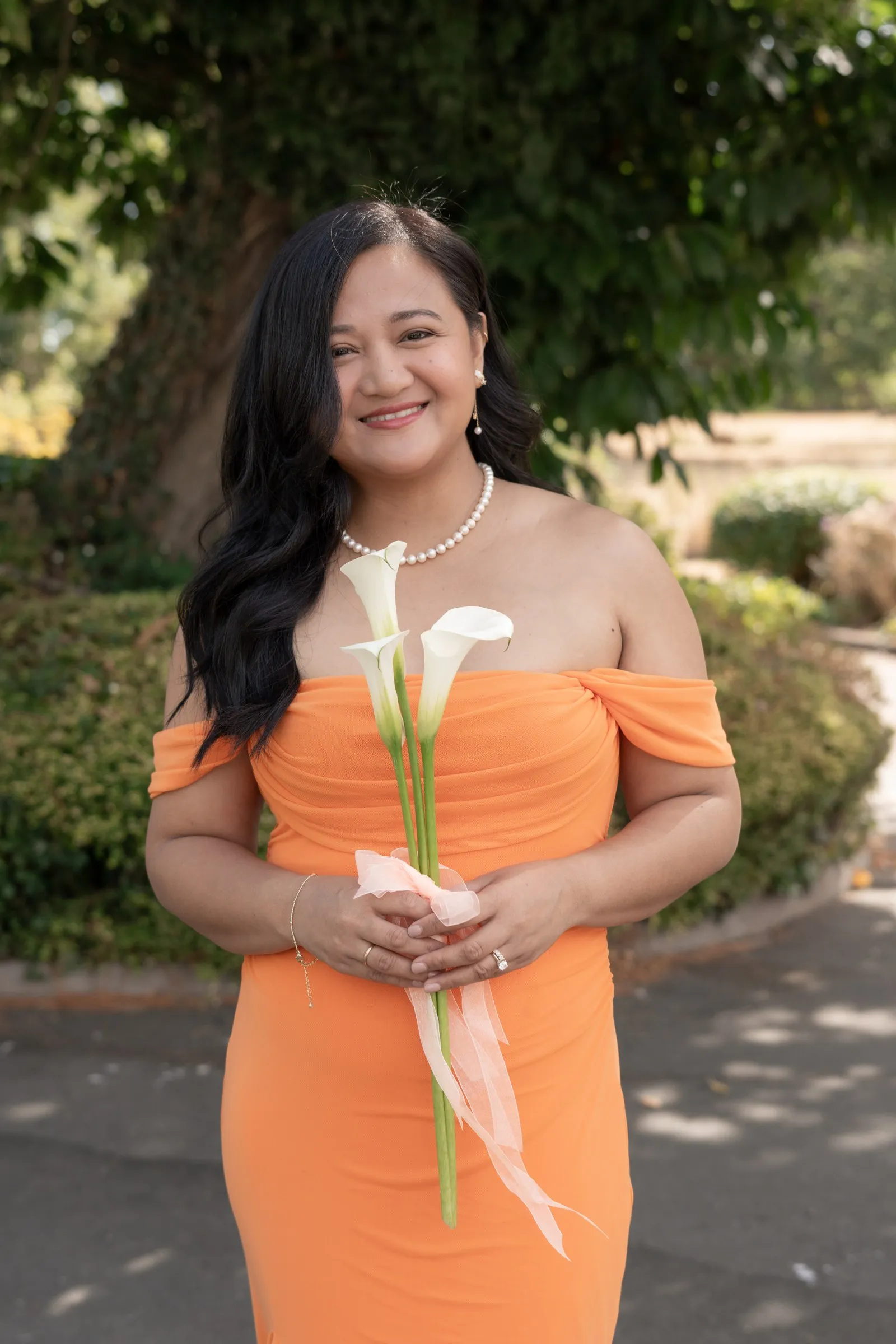 Bridesmaid in a peach off-the-shoulder dress holding calla lilies