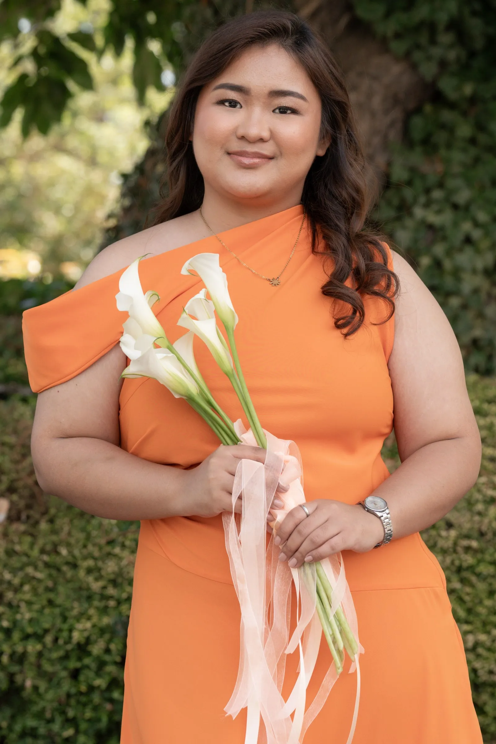Bridesmaid in a peach one-shoulder dress holding calla lilies