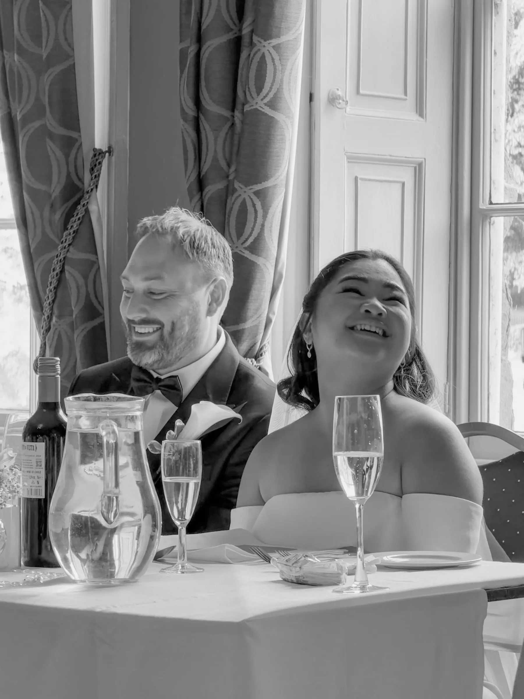 Black and white frame of Mitch and Mathelle laughing at the head table