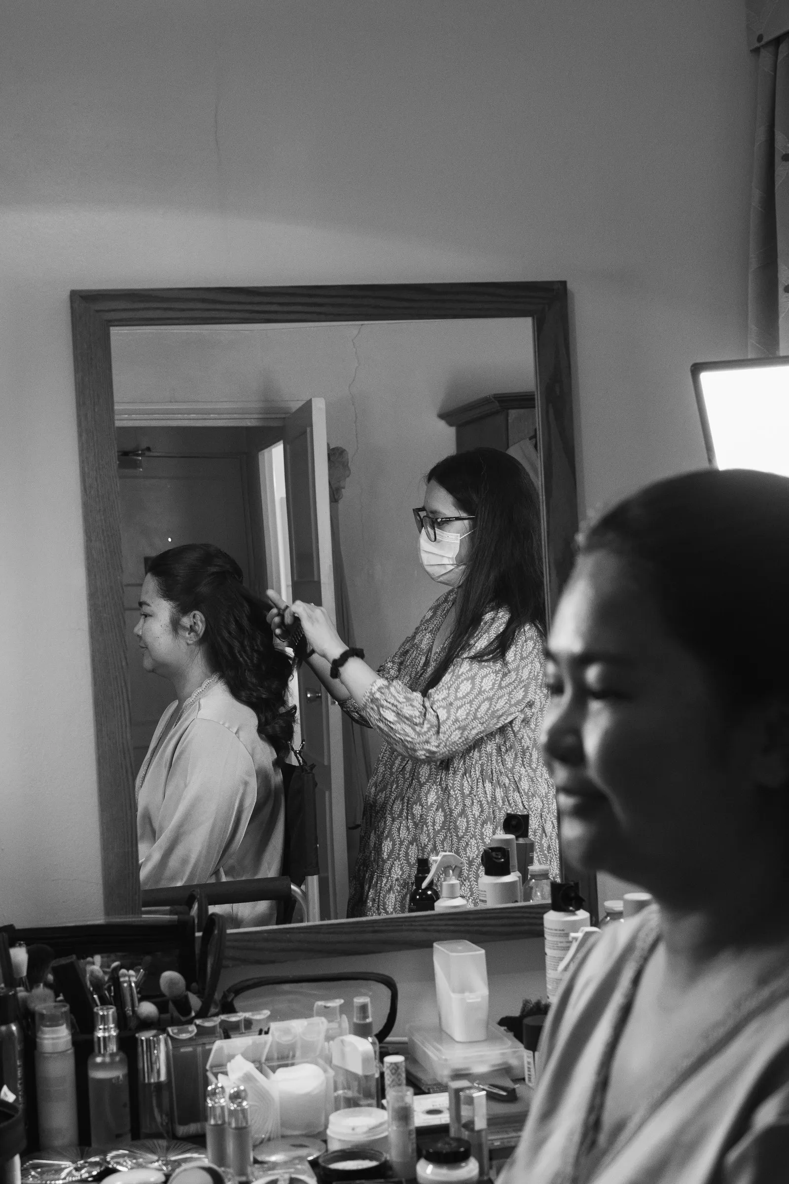 Black and white frame of a hairstylist curling hair, reflected in the bridal suite mirror