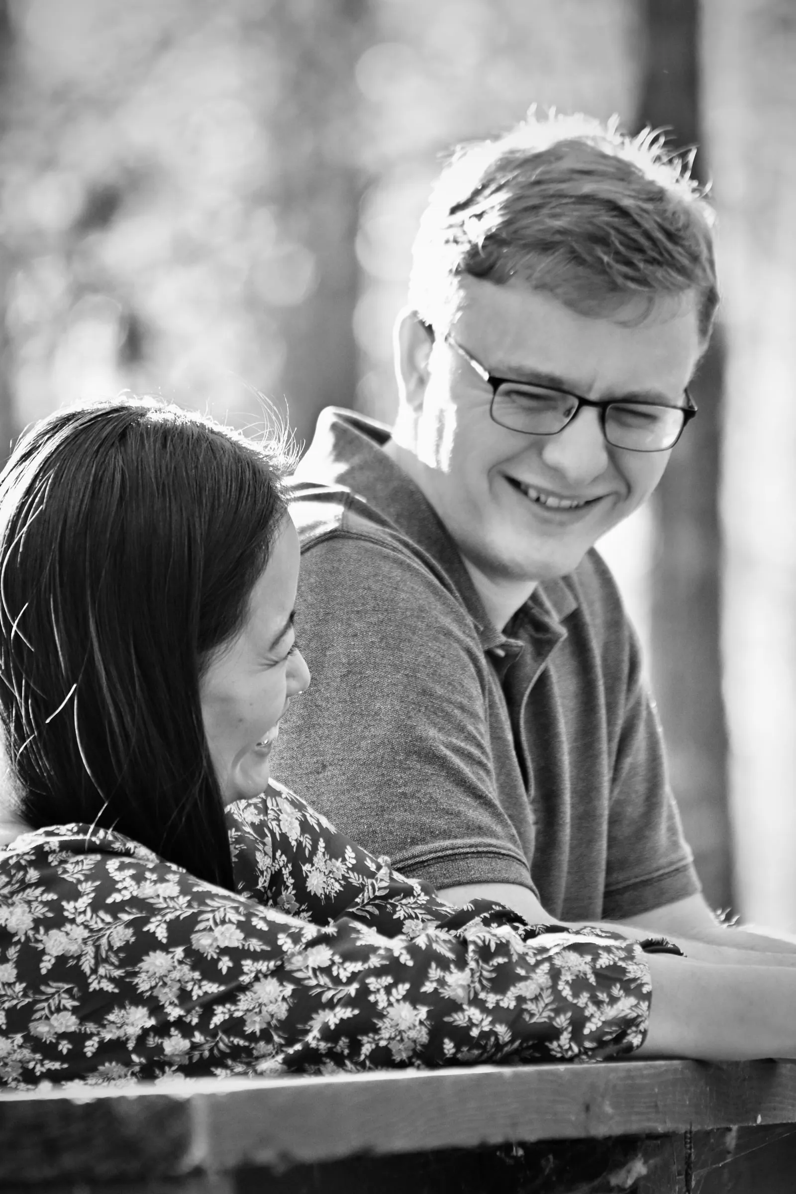 Black and white frame of Jacob smiling down at Mya as they lean on the wooden rail