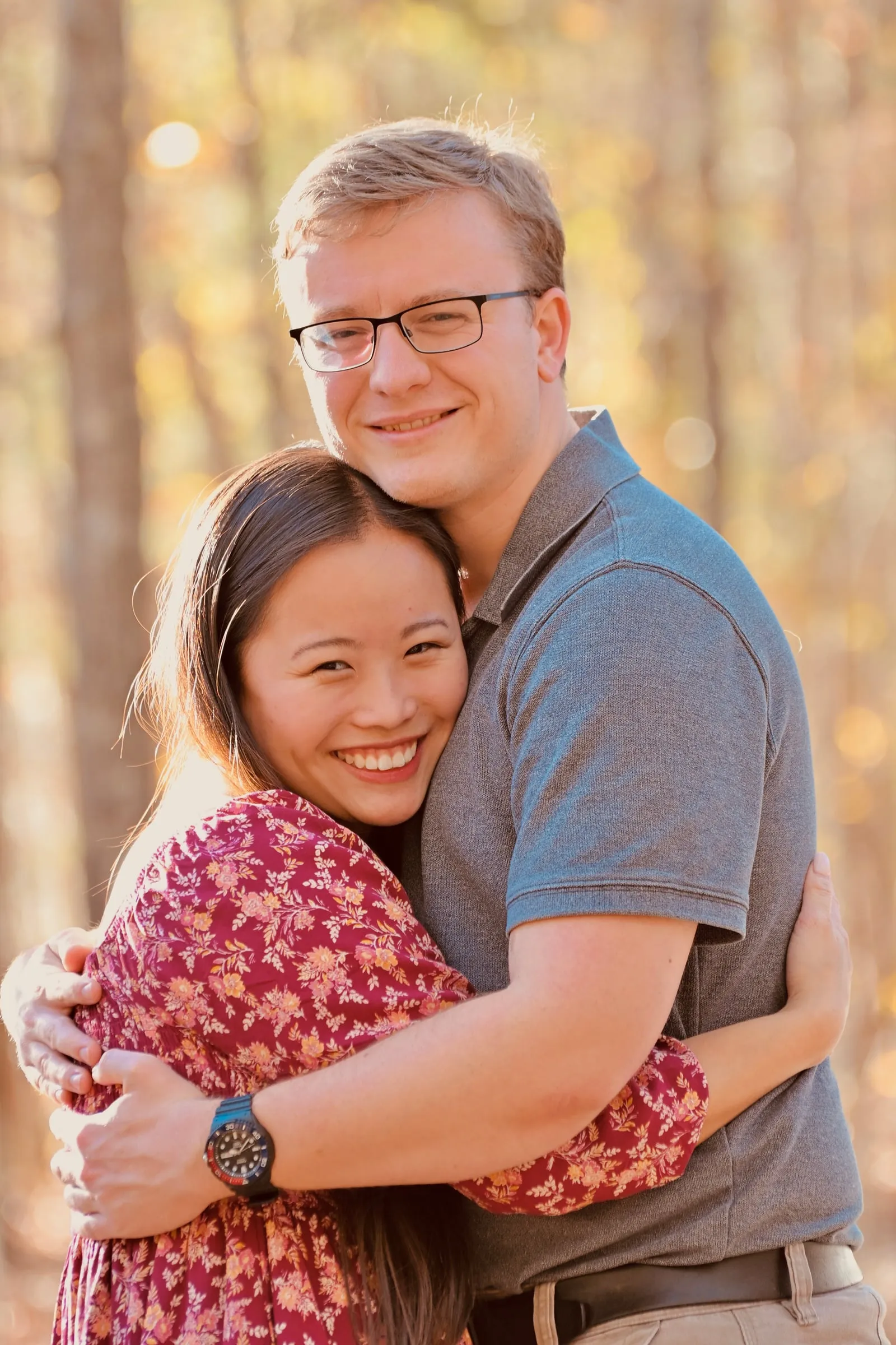 Mya hugging Jacob, both smiling at the camera, warm light coming through the trees