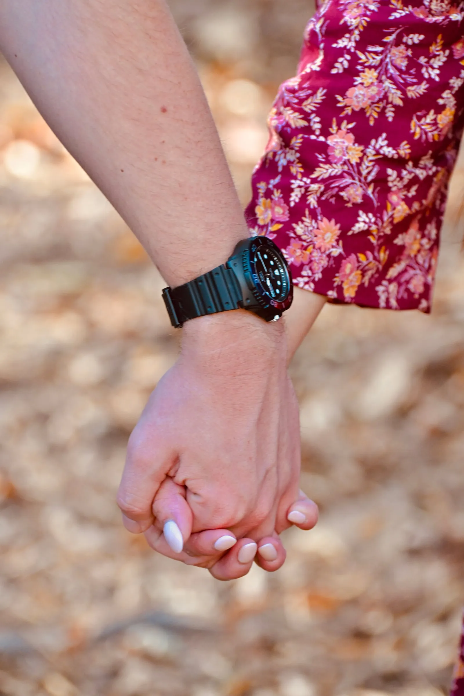 Close-up of Mya and Jacob holding hands, his black watch against her burgundy floral sleeve