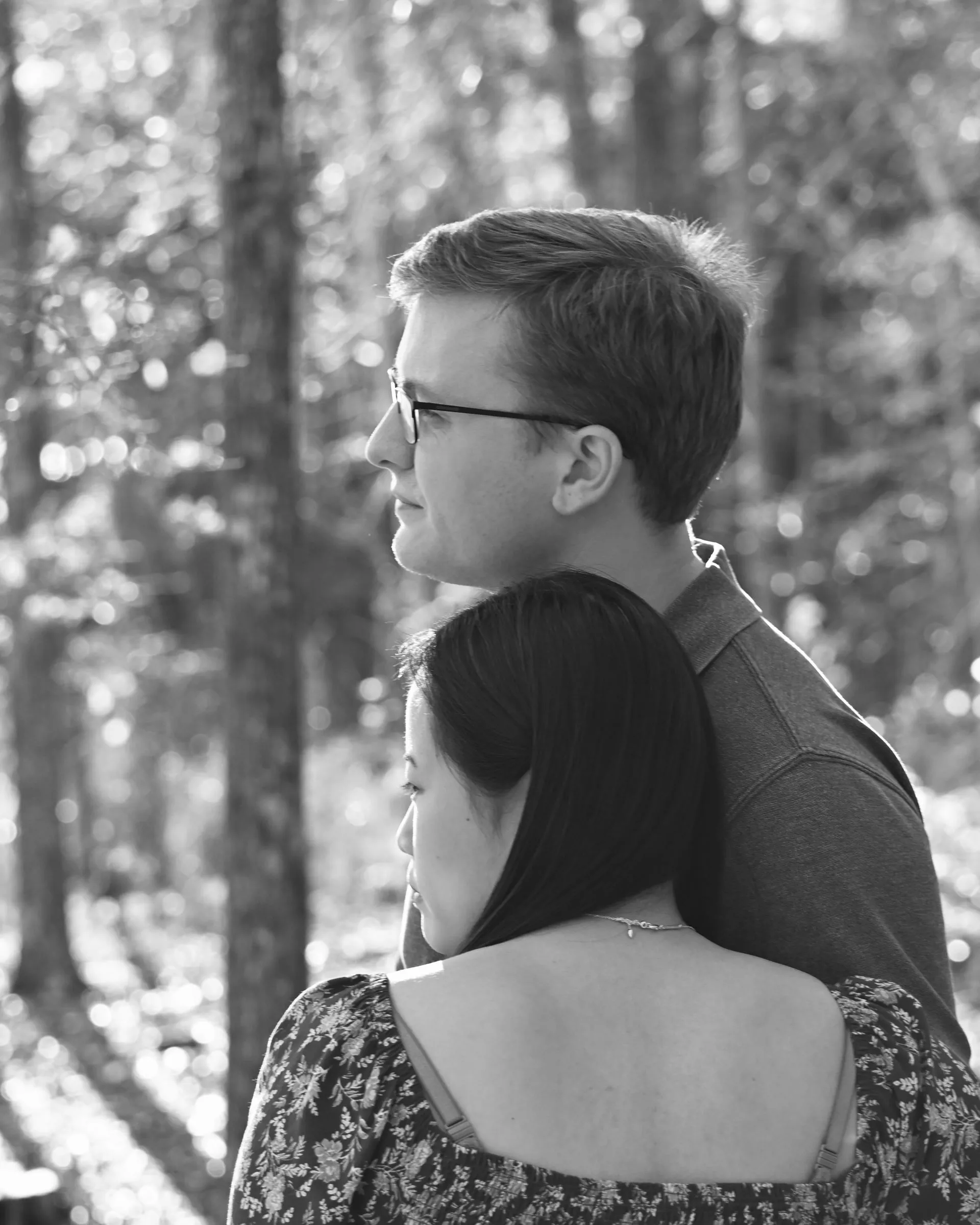 Black and white frame of Mya leaning back against Jacob as they both look off through the trees
