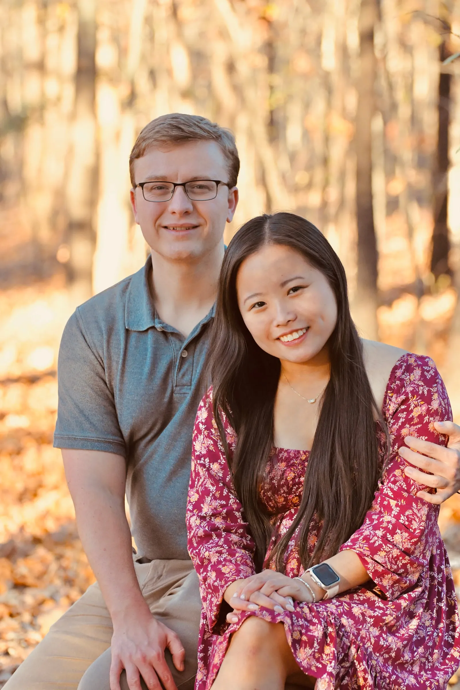 Mya and Jacob seated close together, smiling at the camera in front of golden woods