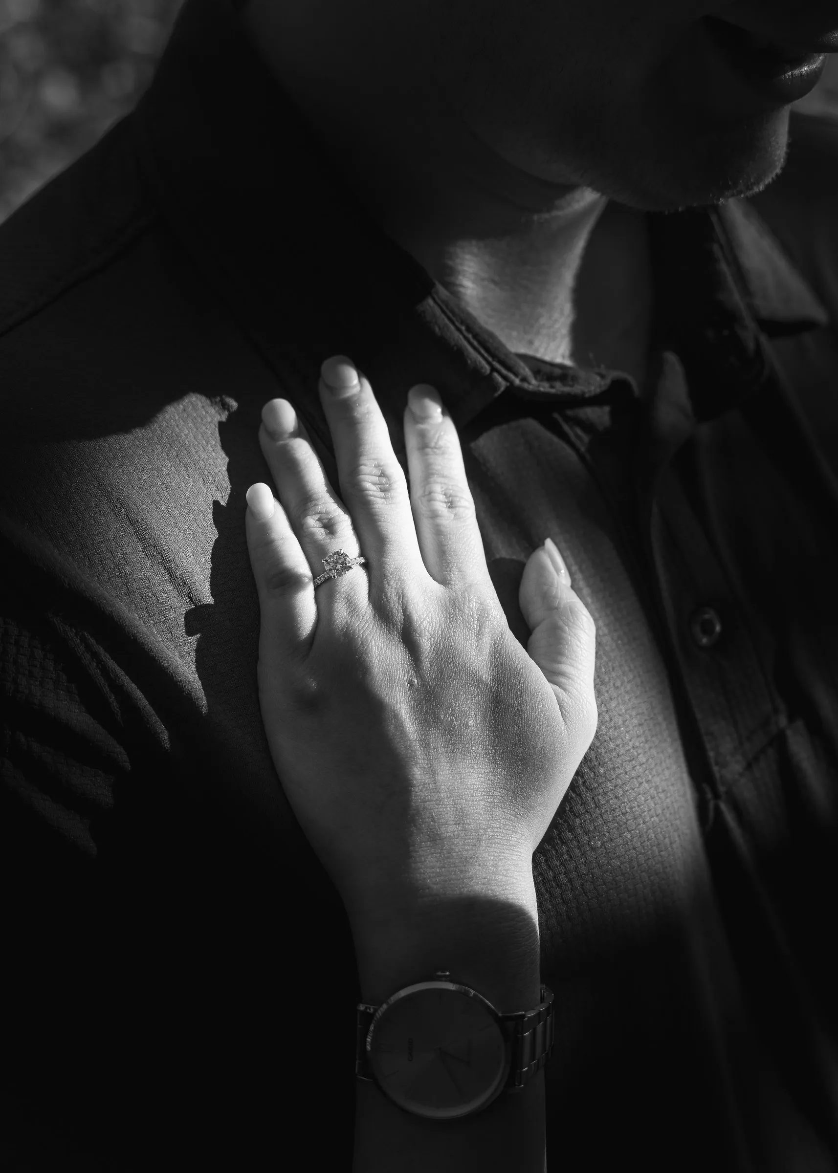 Black and white close-up of Mya's hand and engagement ring resting on Jacob's chest