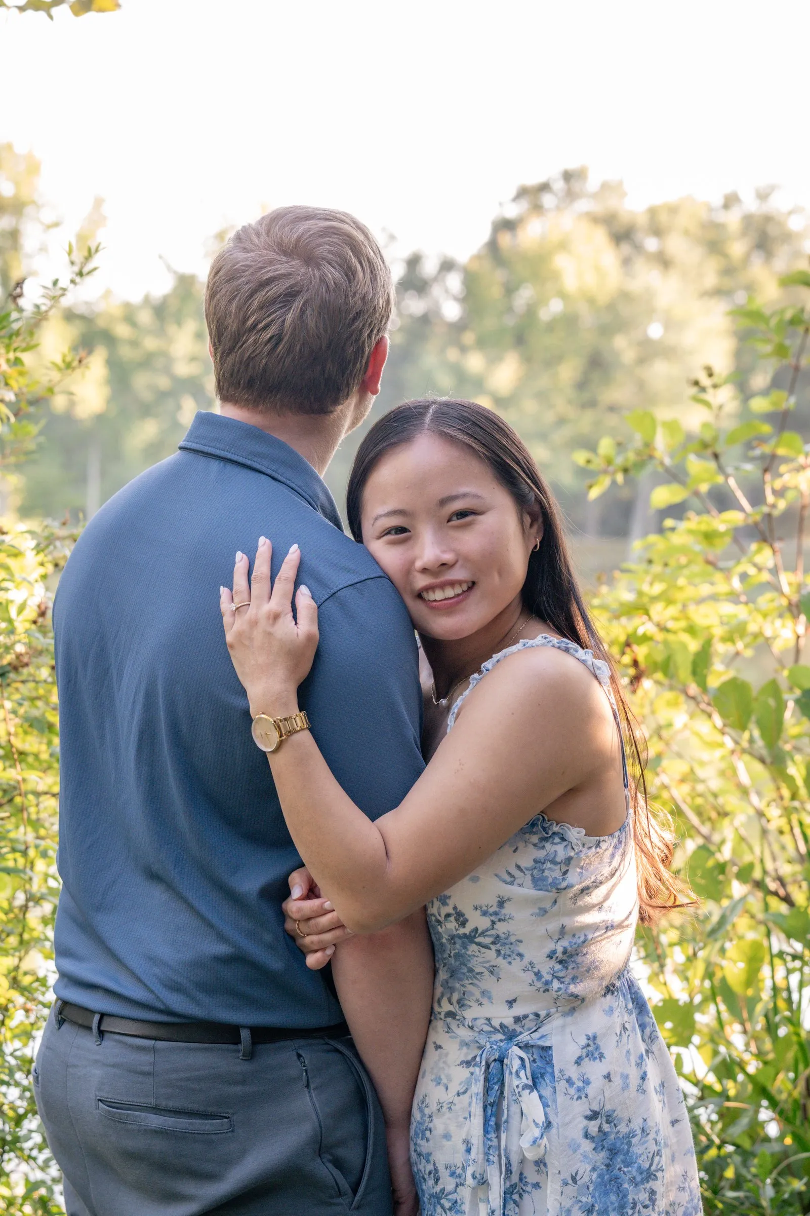 Mya with her arms around Jacob's neck, smiling at the camera among green trees