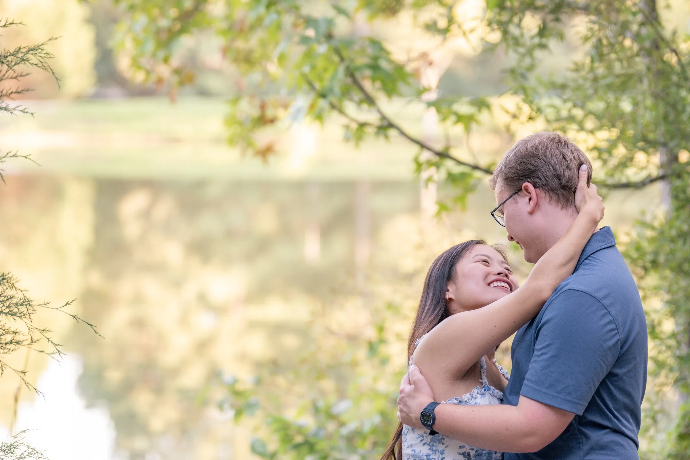 Mya and Jacob embracing beside the pond, trees reflected in the water