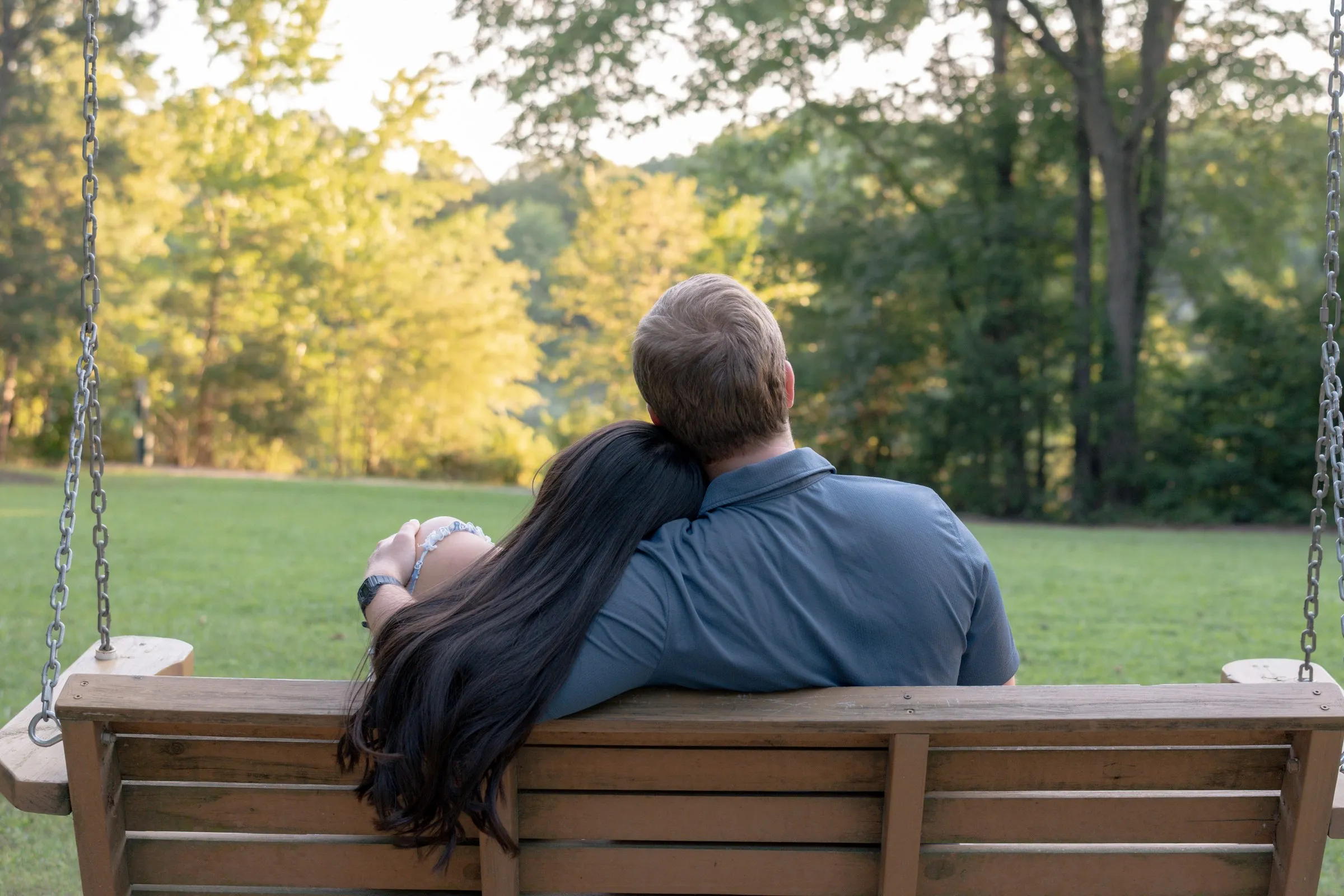 Mya and Jacob seen from behind on a wooden porch swing, looking out at the trees