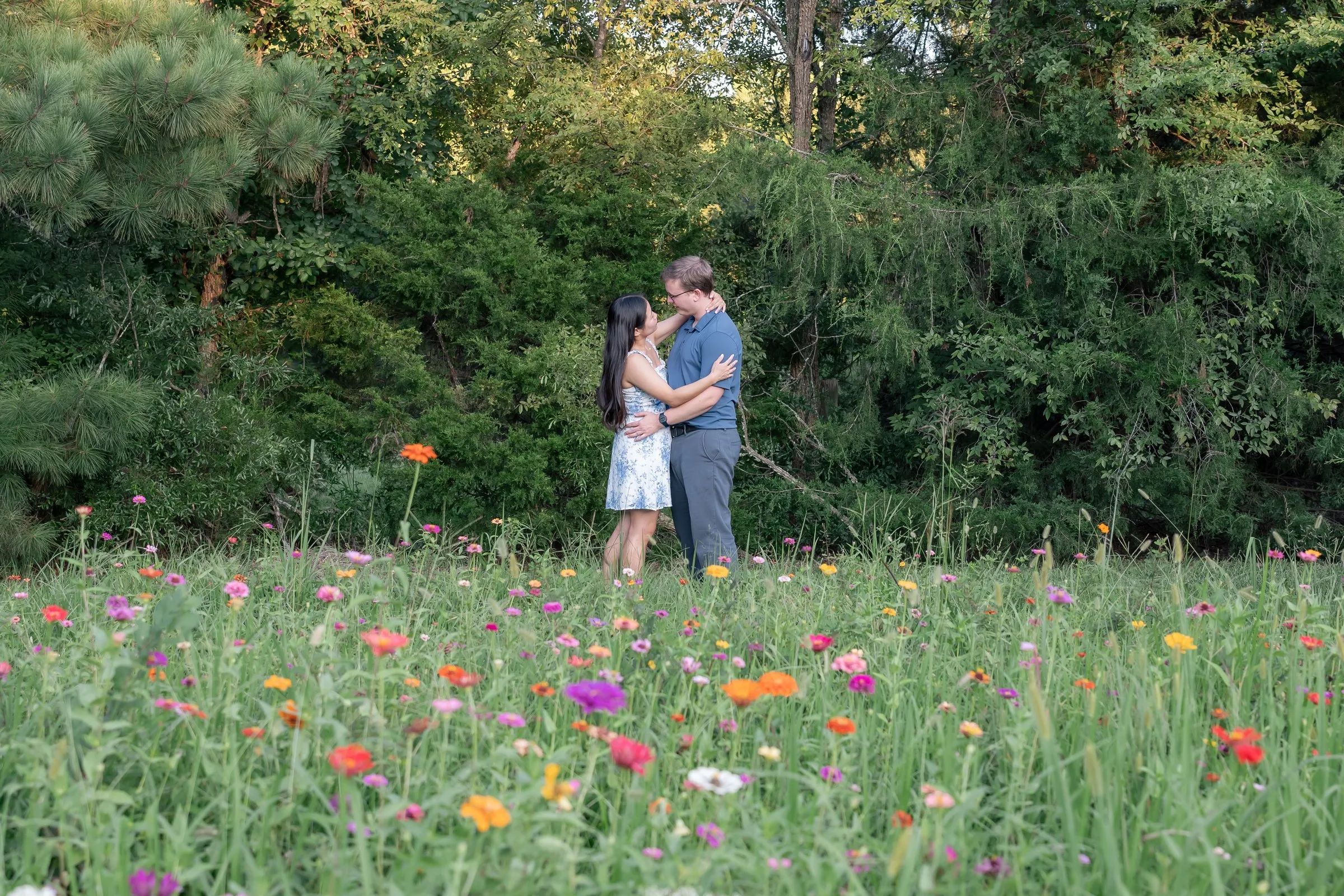 Wide view of Mya and Jacob embracing at the edge of a wildflower field in Waxhaw, NC