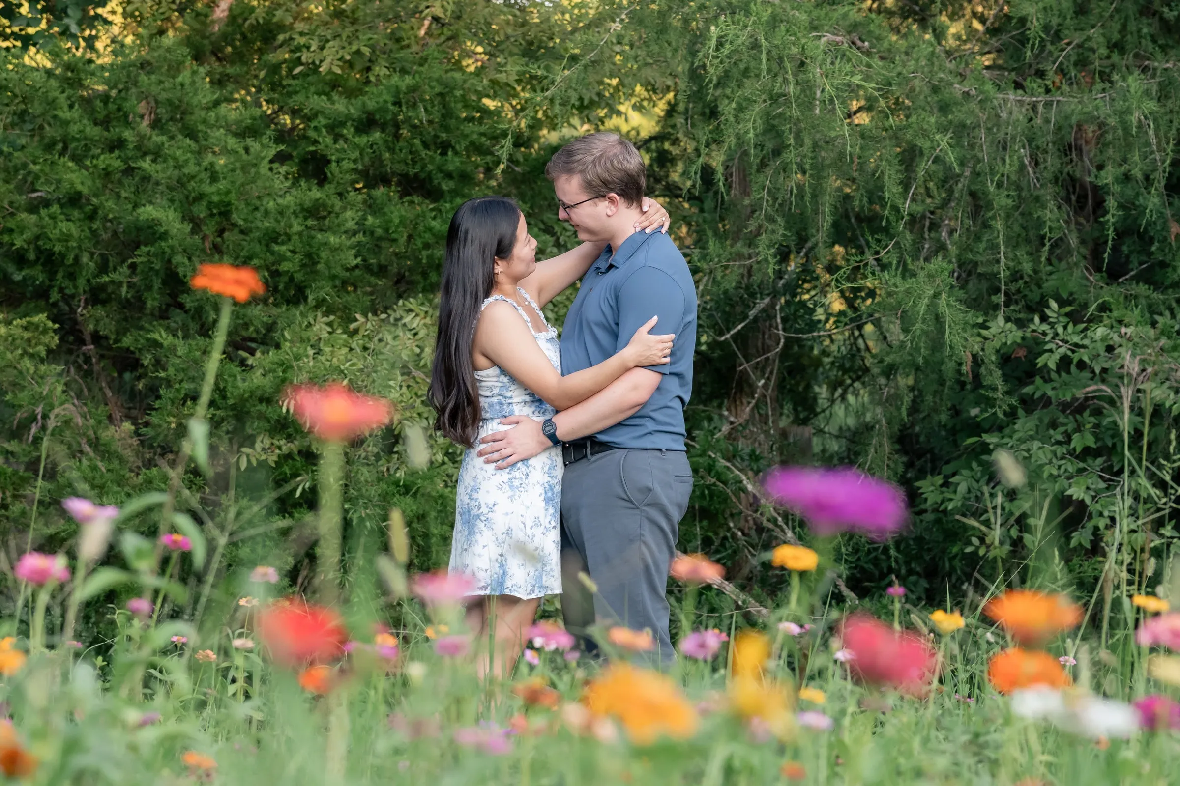 Mya and Jacob embracing among orange, pink and purple zinnias at Marvin Efird Park in Waxhaw, NC