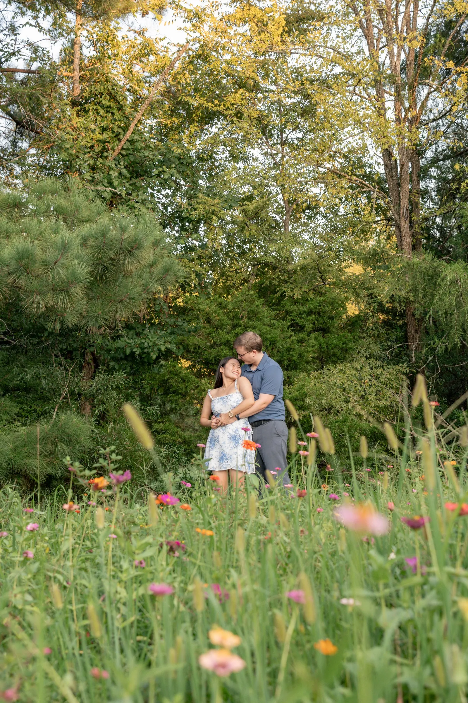 Wide view of Mya and Jacob embracing in tall grass and wildflowers below the tree line