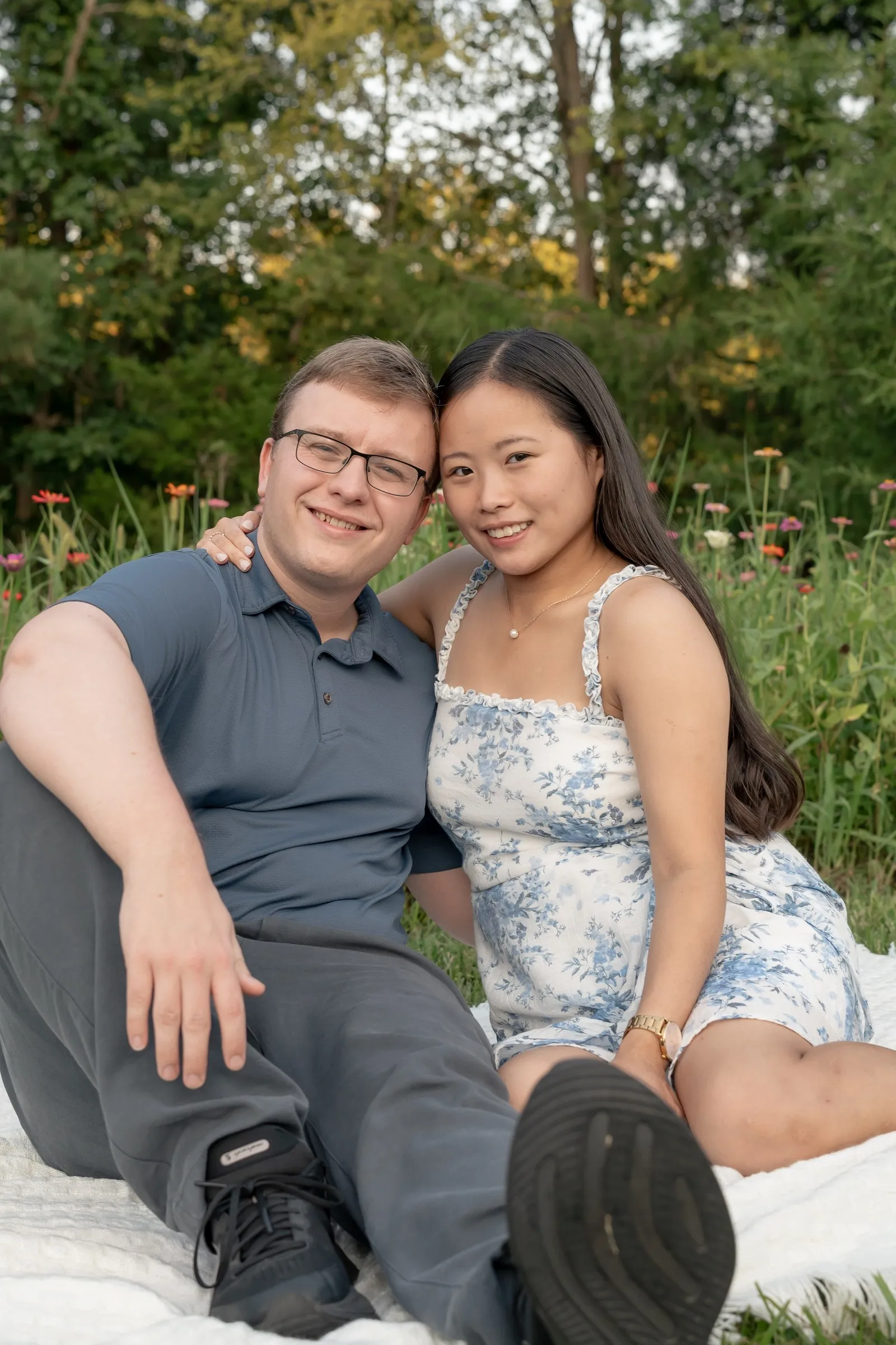 Mya and Jacob seated on a white blanket, smiling at the camera in front of wildflowers