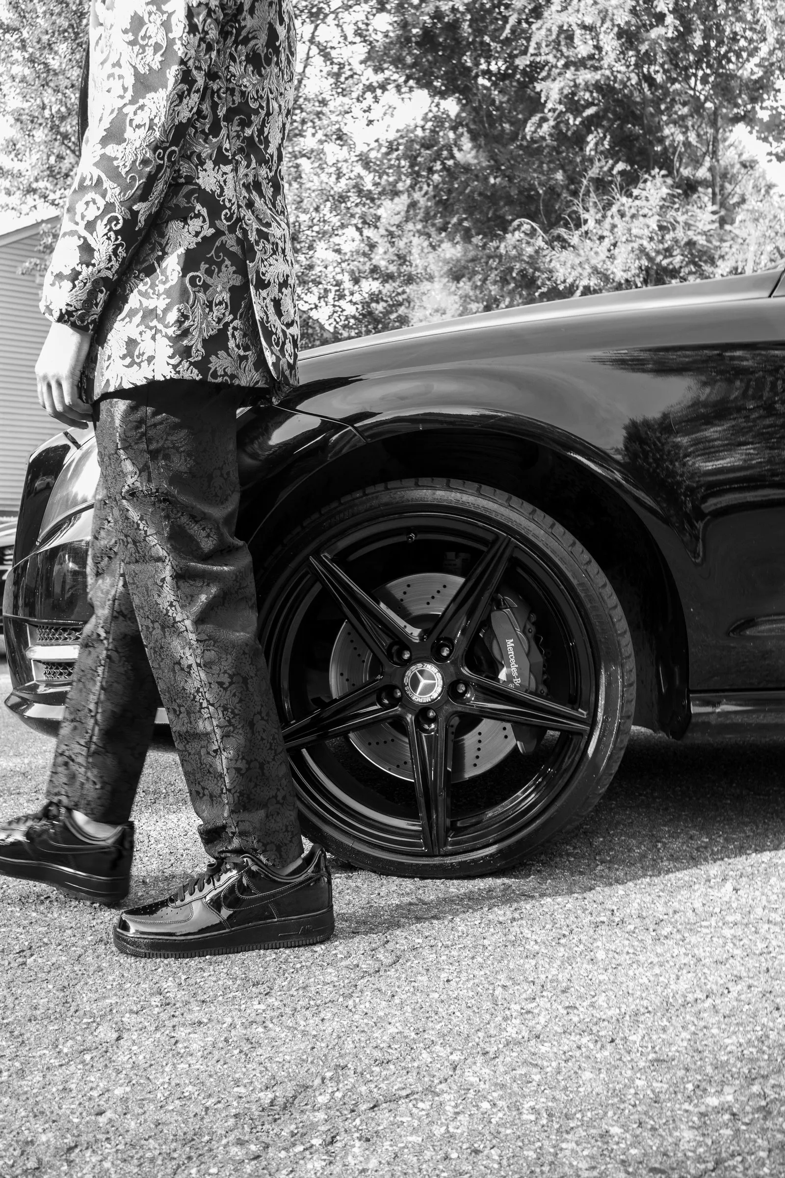 Black and white detail of his shoes and the car's wheel