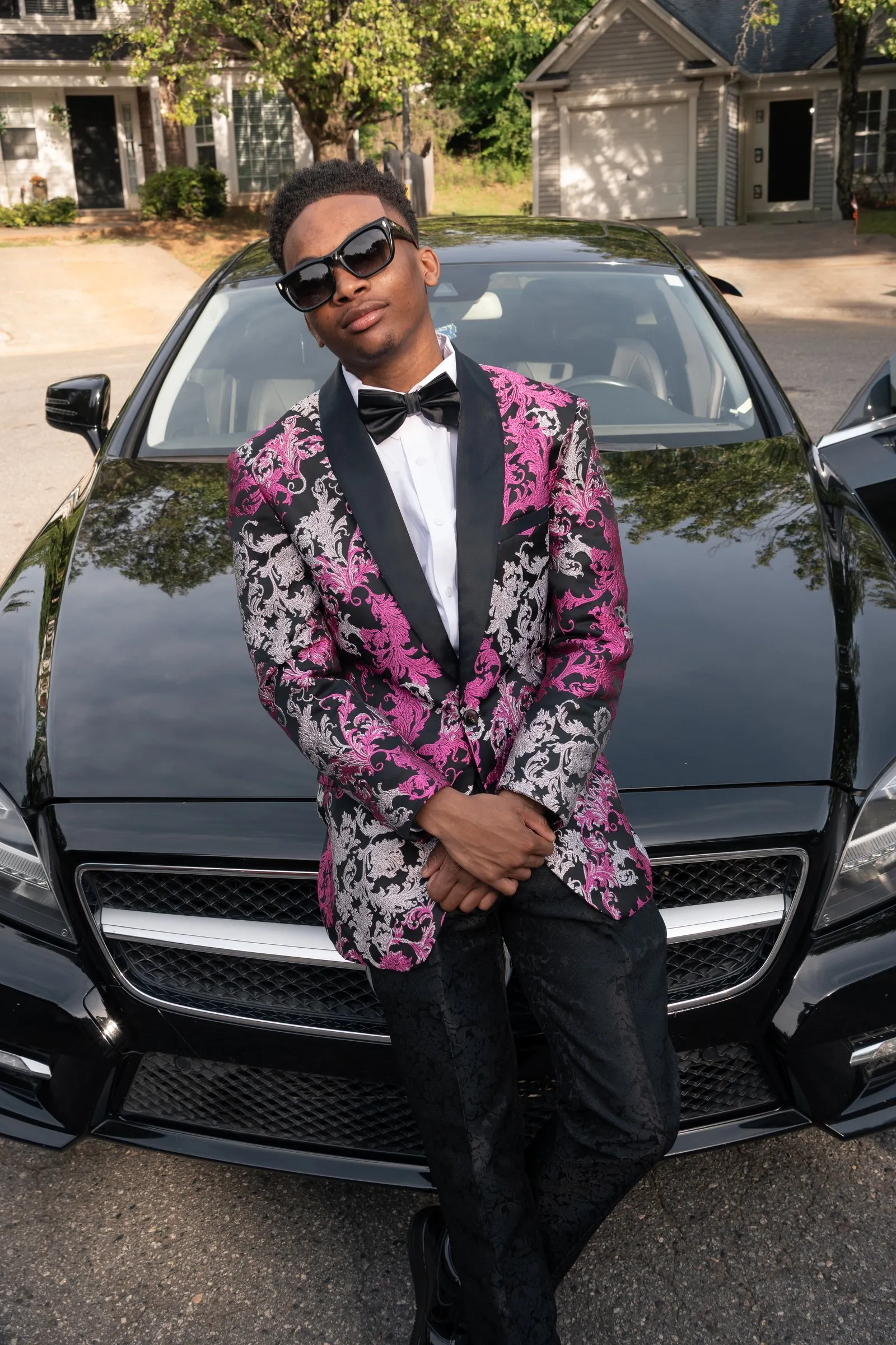 He sits on the hood of the Mercedes, sunglasses on