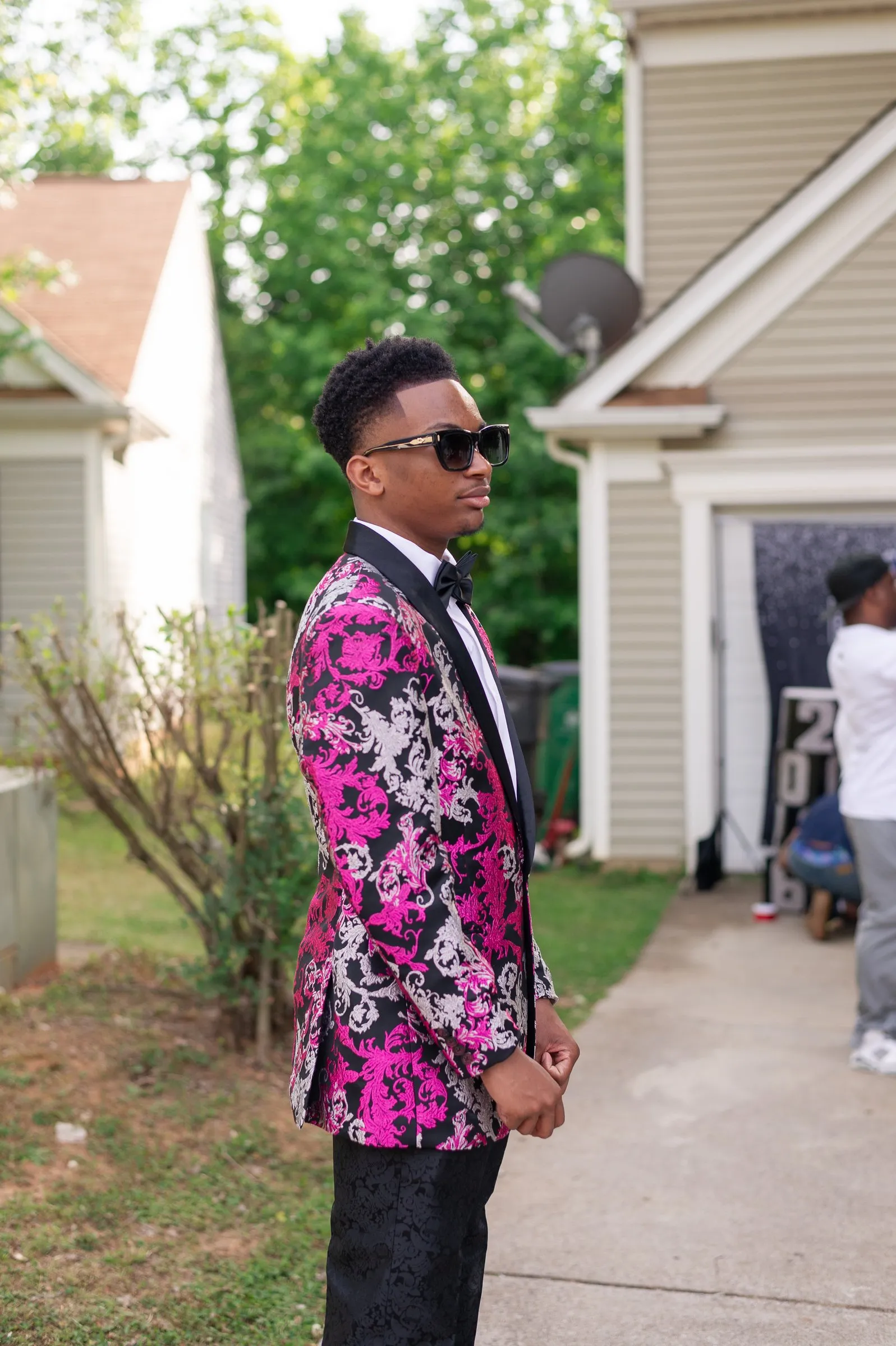He stands in the driveway in a pink and silver floral tuxedo jacket and sunglasses before the send-off