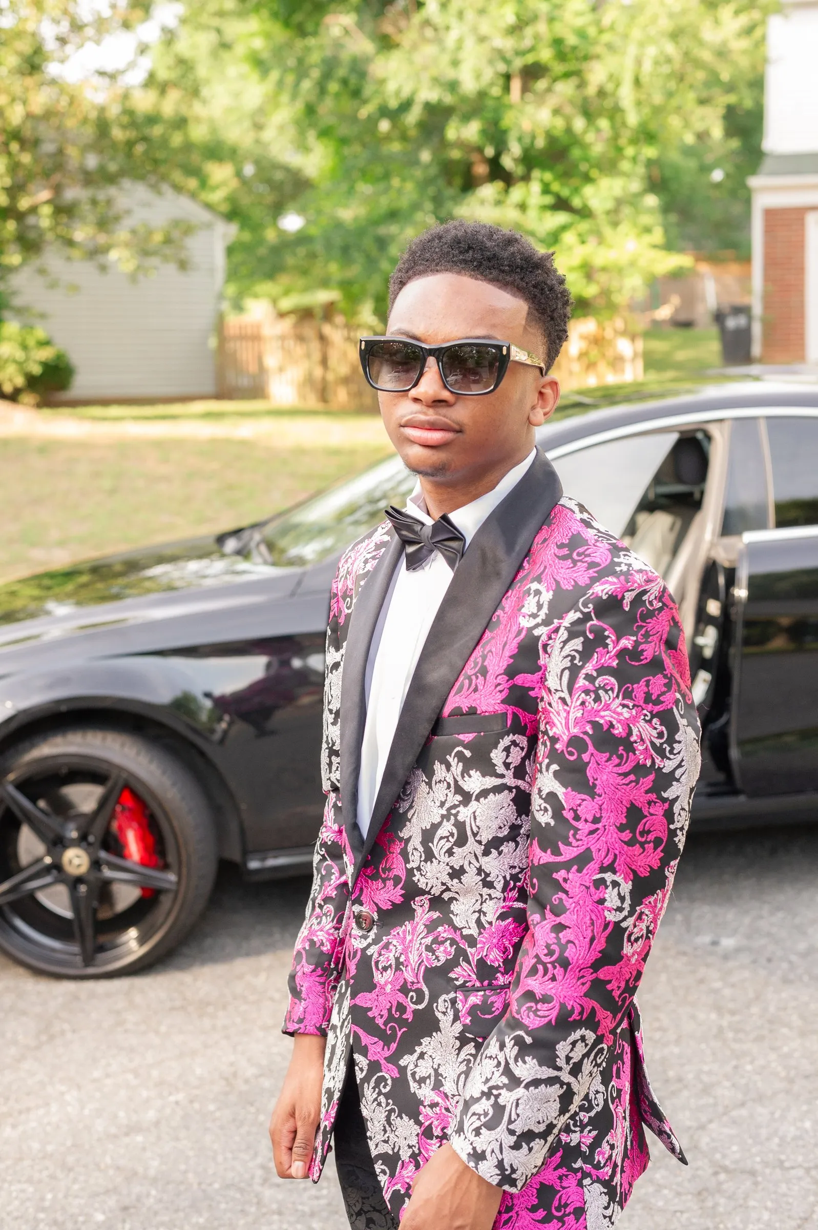 Three quarter portrait in his pink floral tuxedo jacket beside a black sports car