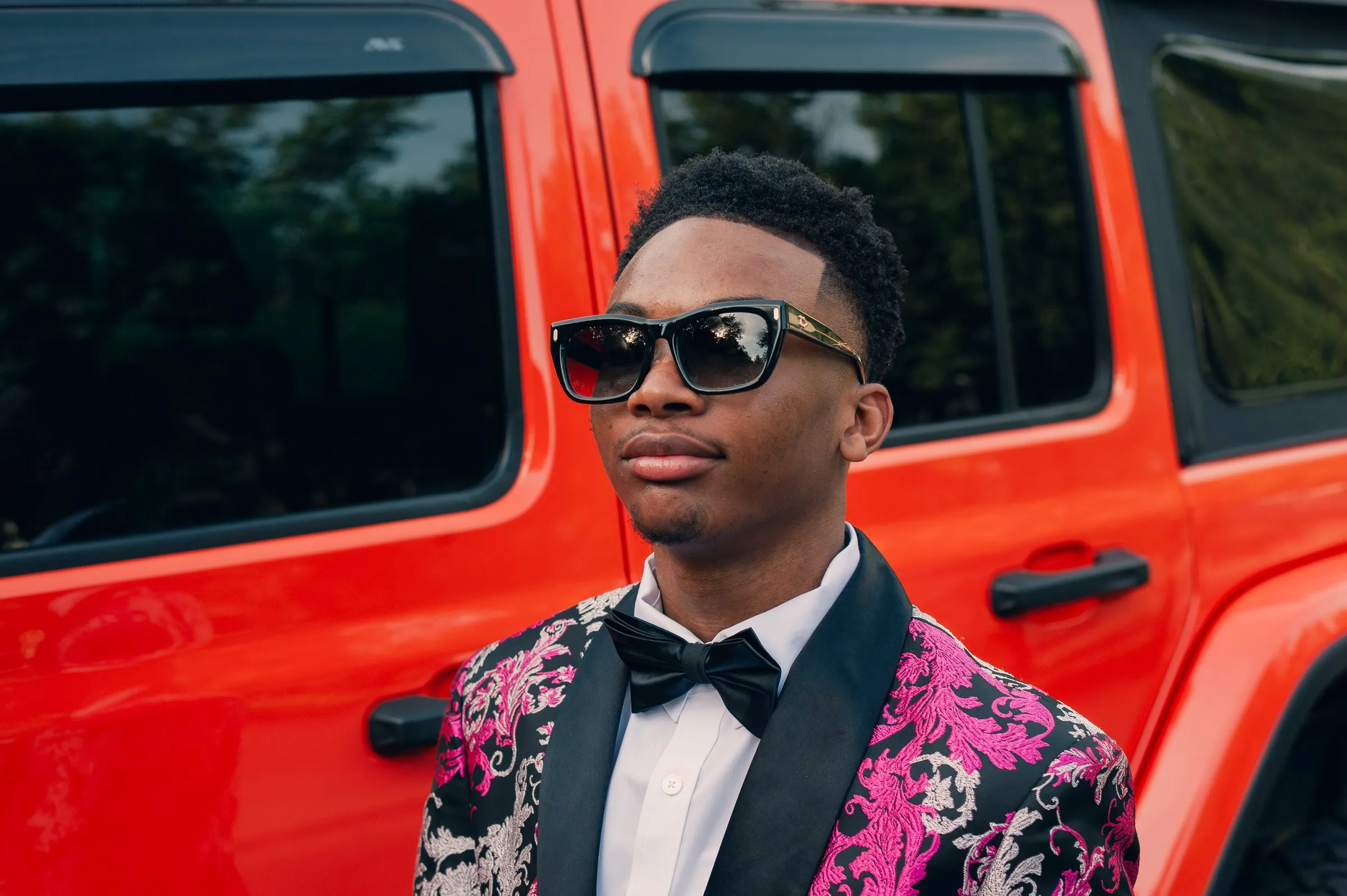 Portrait in sunglasses and a black bow tie against the door of an orange Jeep Wrangler
