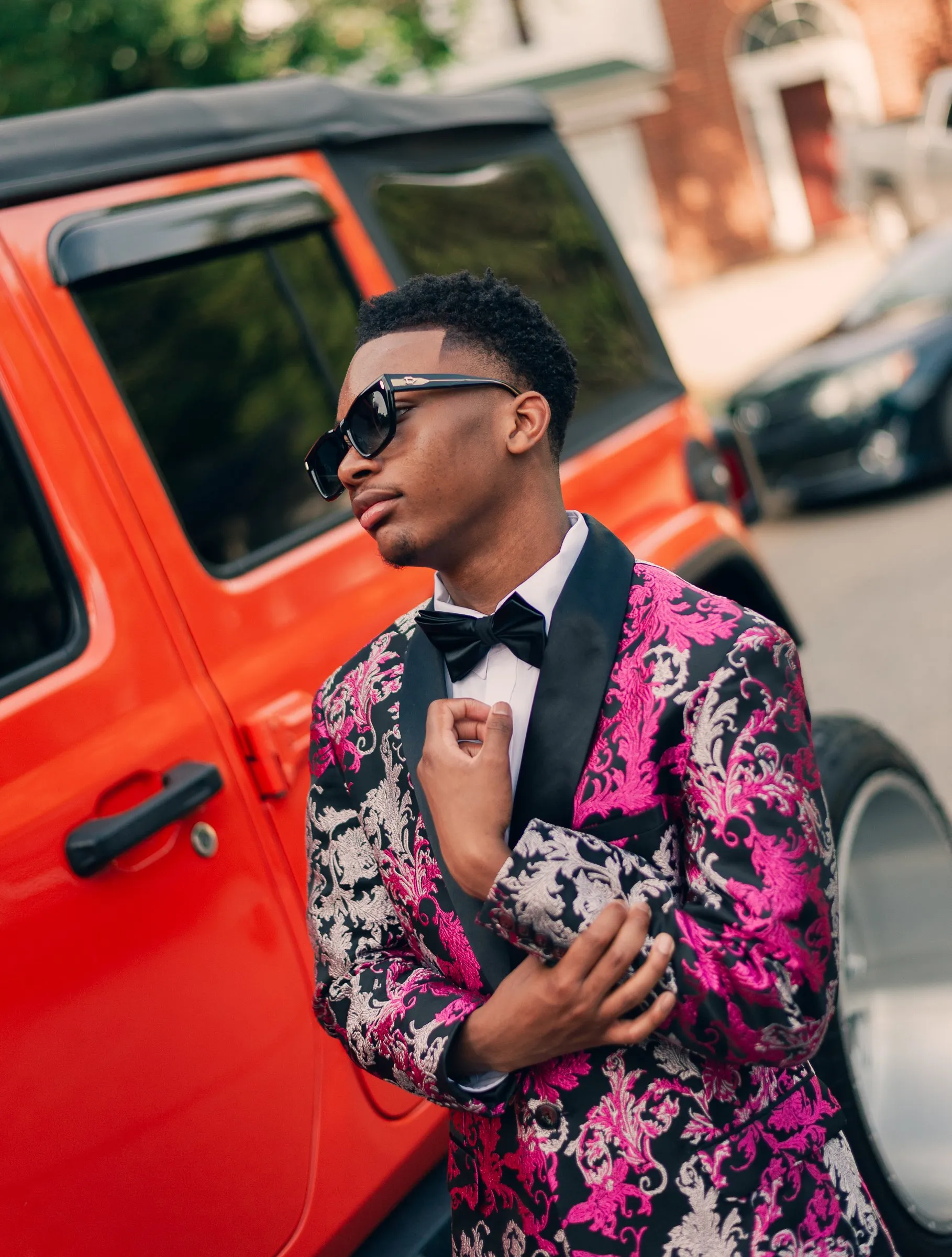 He adjusts his jacket cuff in front of the orange Jeep Wrangler