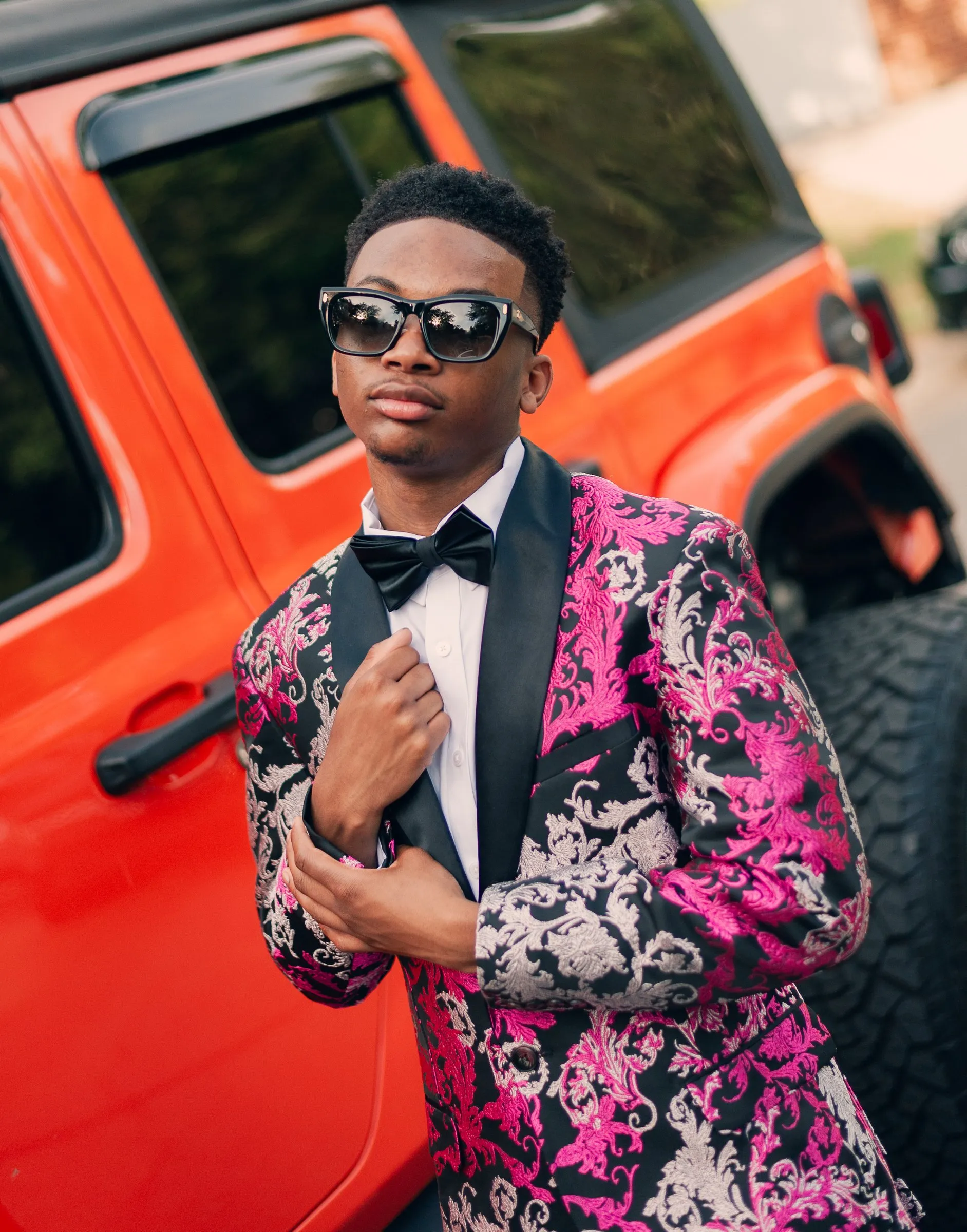 He fixes his cuff against the bright orange Jeep, sunglasses on
