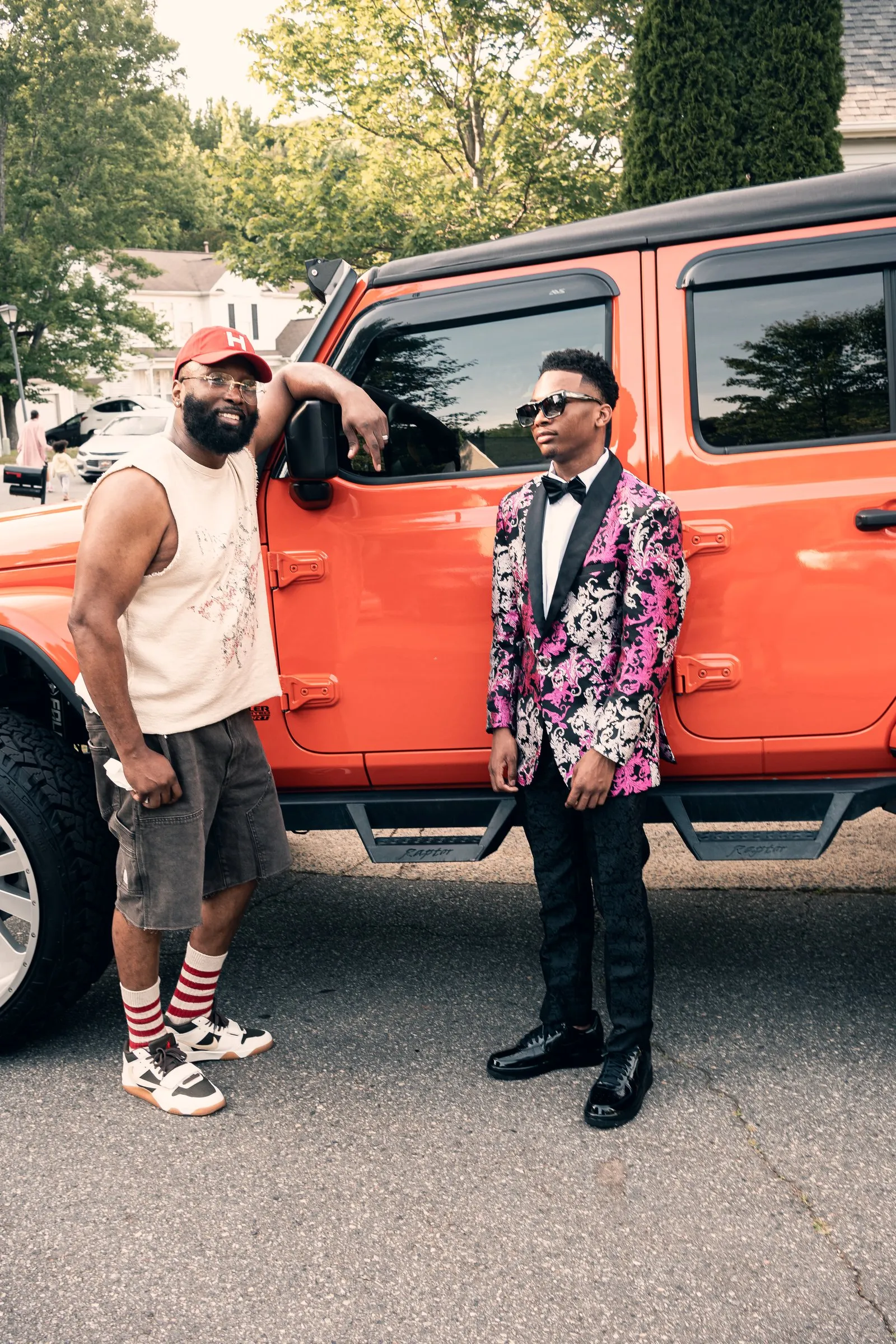 He poses with a man in a red cap beside the orange Jeep Wrangler