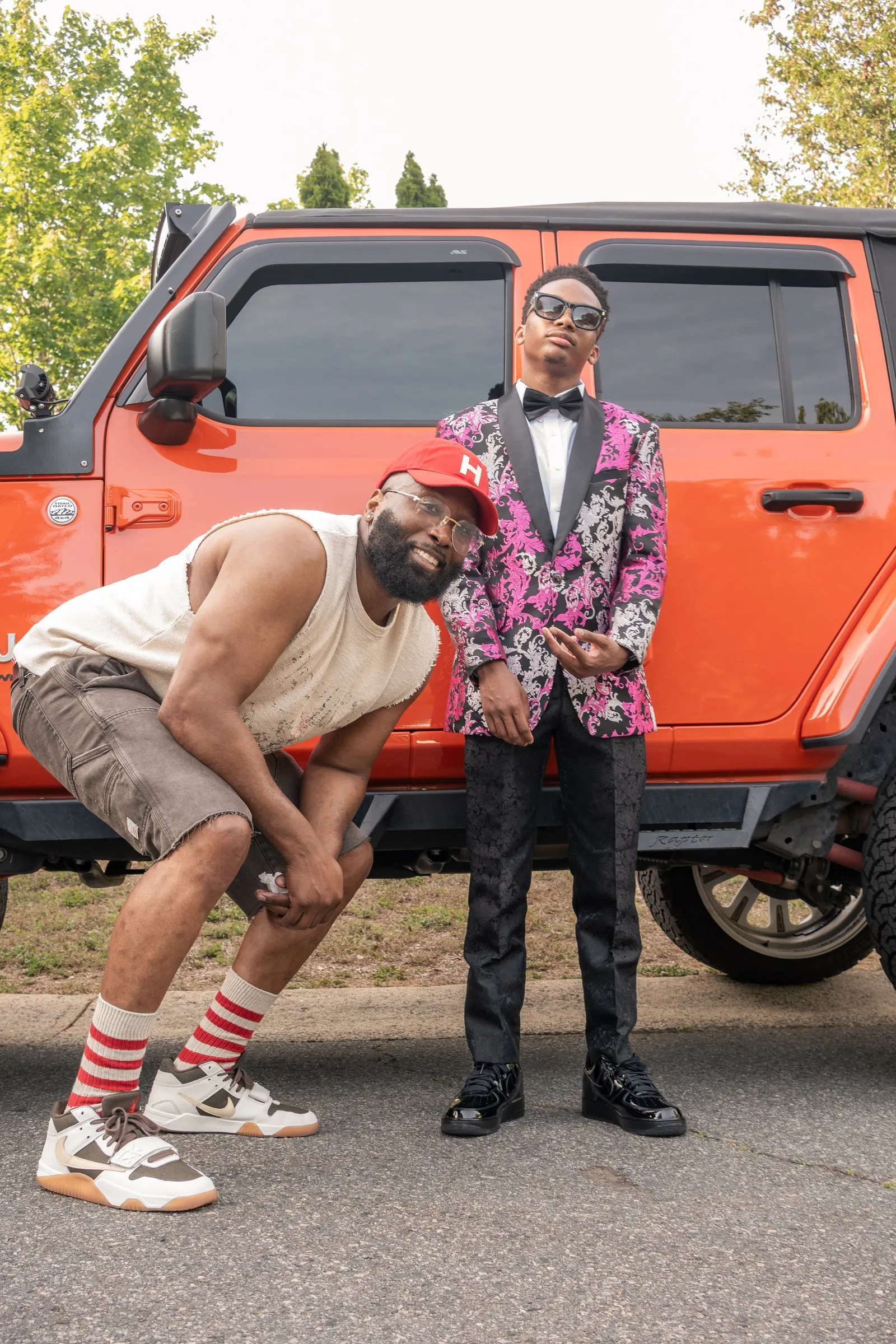 He poses with a man in a red cap in front of the orange Jeep