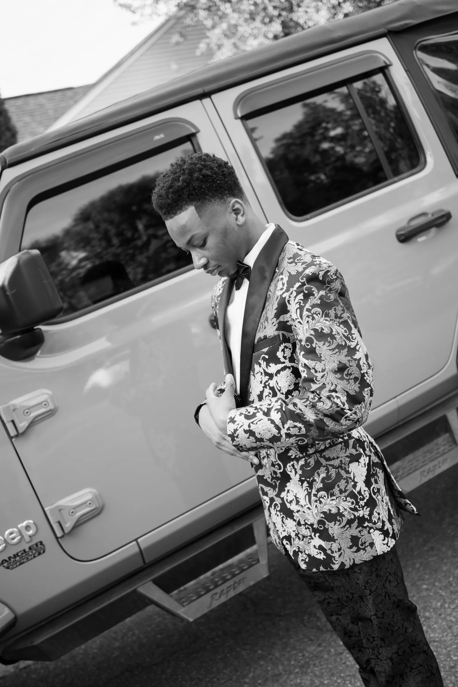 Black and white photograph of him looking down to fix his cuff against the Jeep