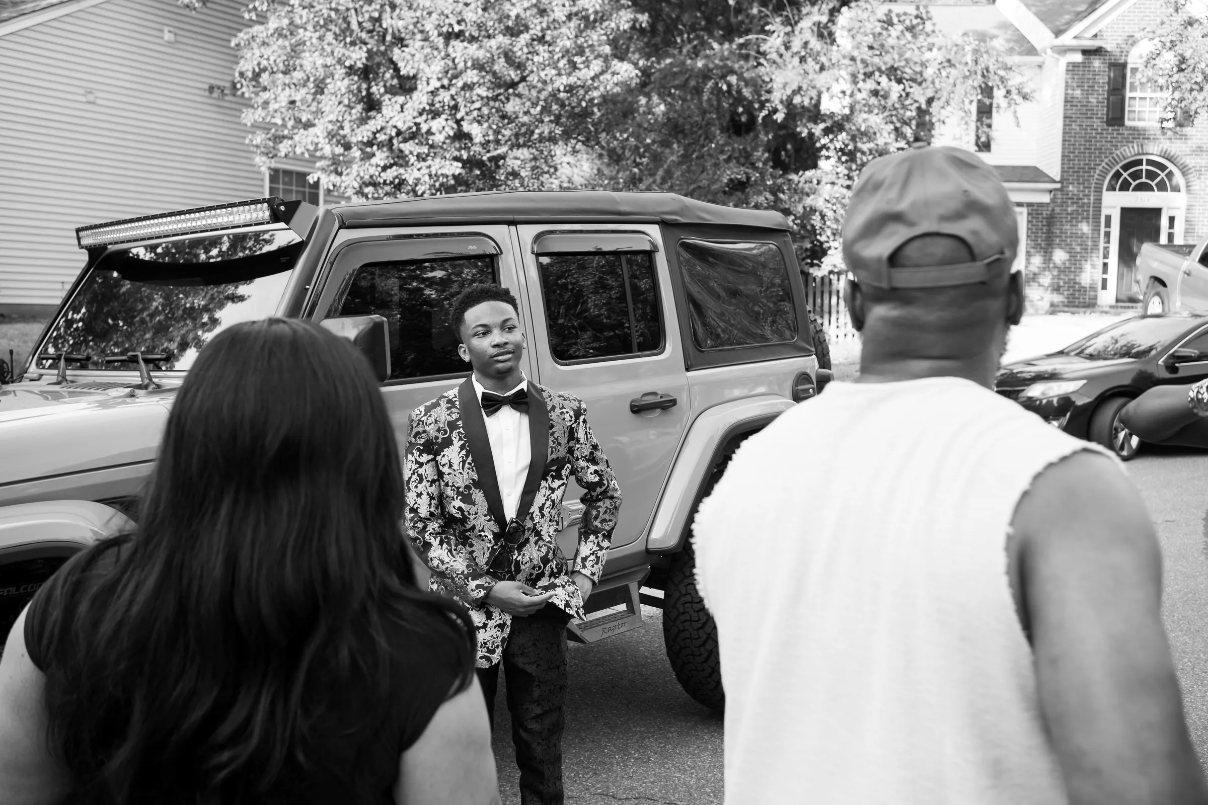 Black and white photograph of family looking on as he poses by the Jeep