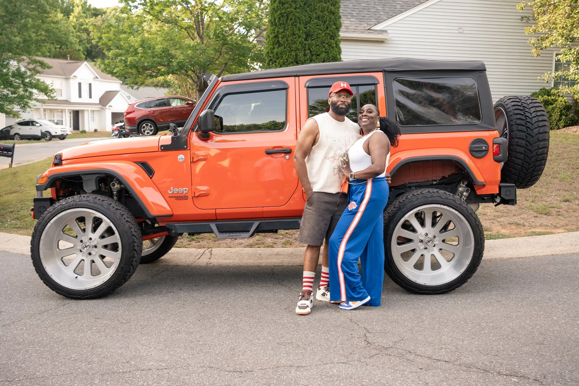 A couple poses in front of the orange Jeep