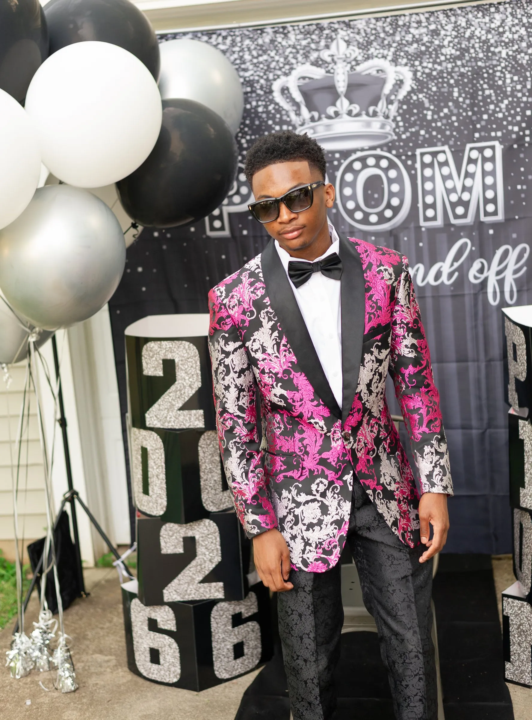 Full length prom portrait in front of the send-off backdrop, black, white, and silver balloons, and the 2026 blocks