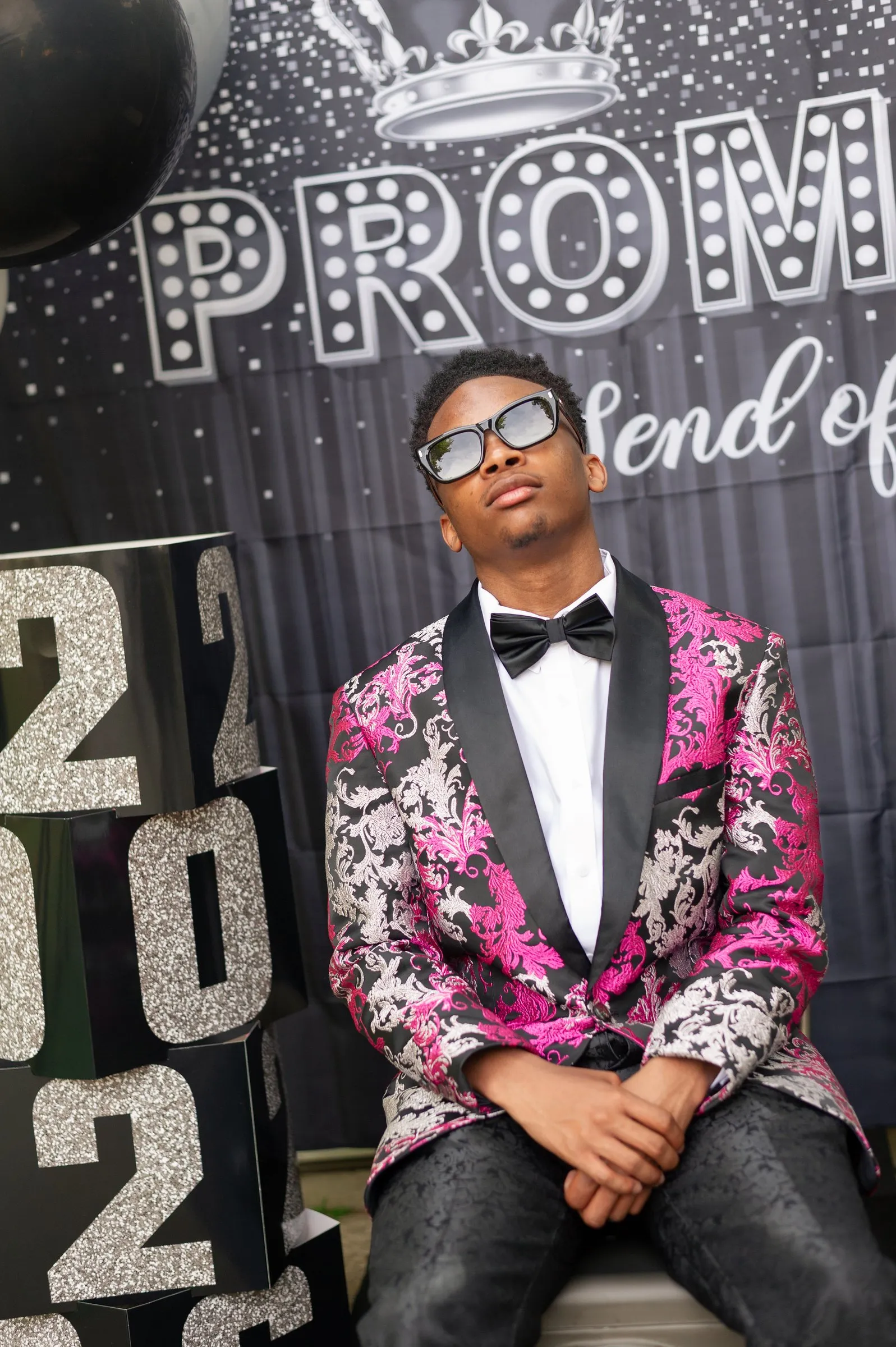Seated prom portrait in sunglasses in front of the send-off backdrop and 2026 blocks