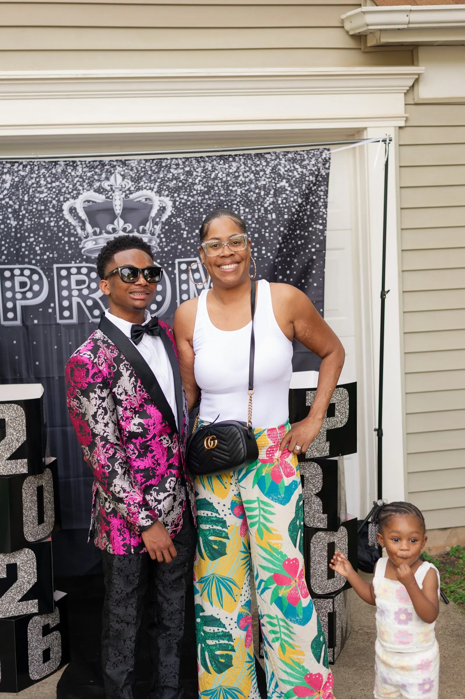 He poses with a woman in tropical print pants and a little girl in front of the send-off backdrop