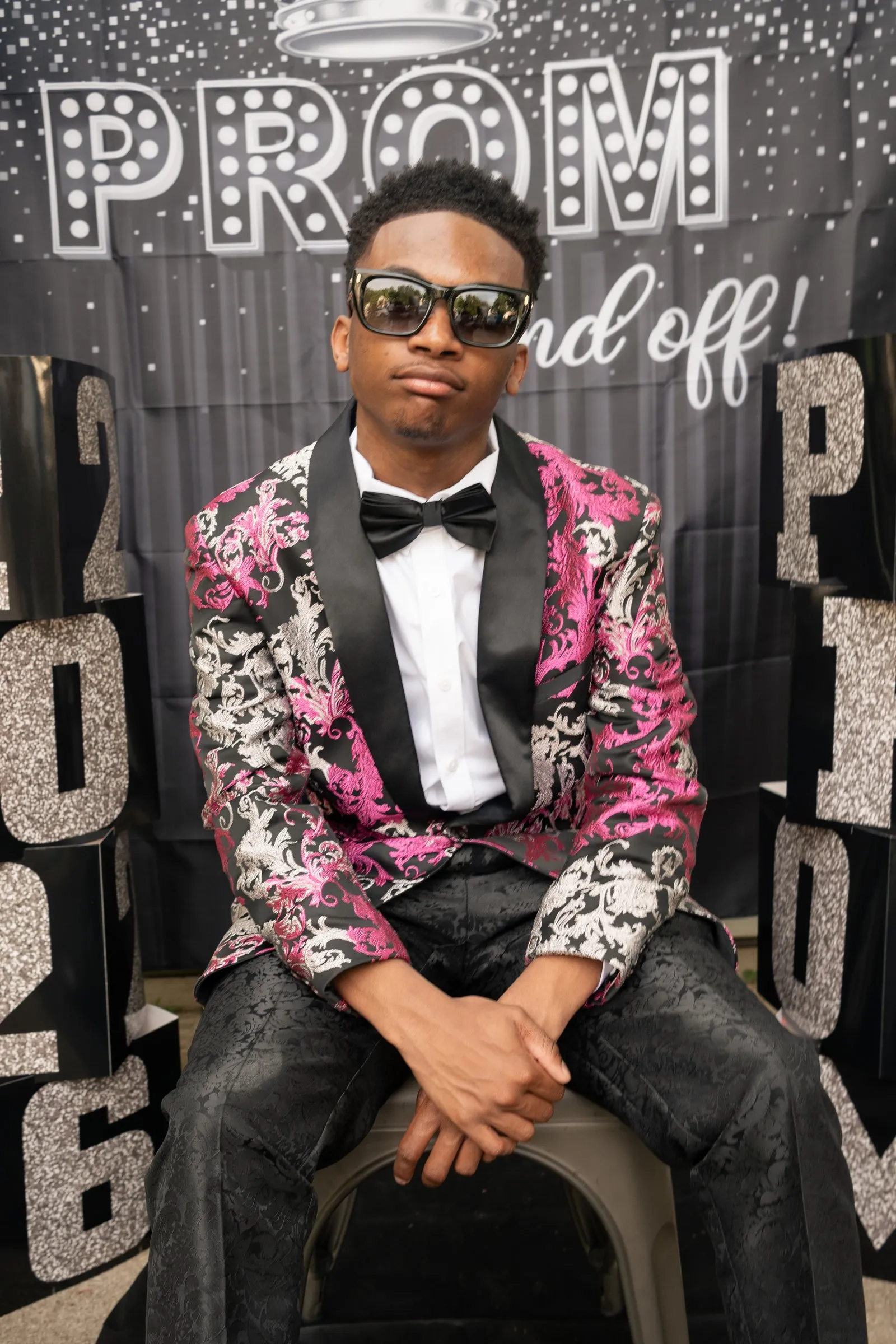 Seated prom portrait in sunglasses in front of the Prom Send Off backdrop