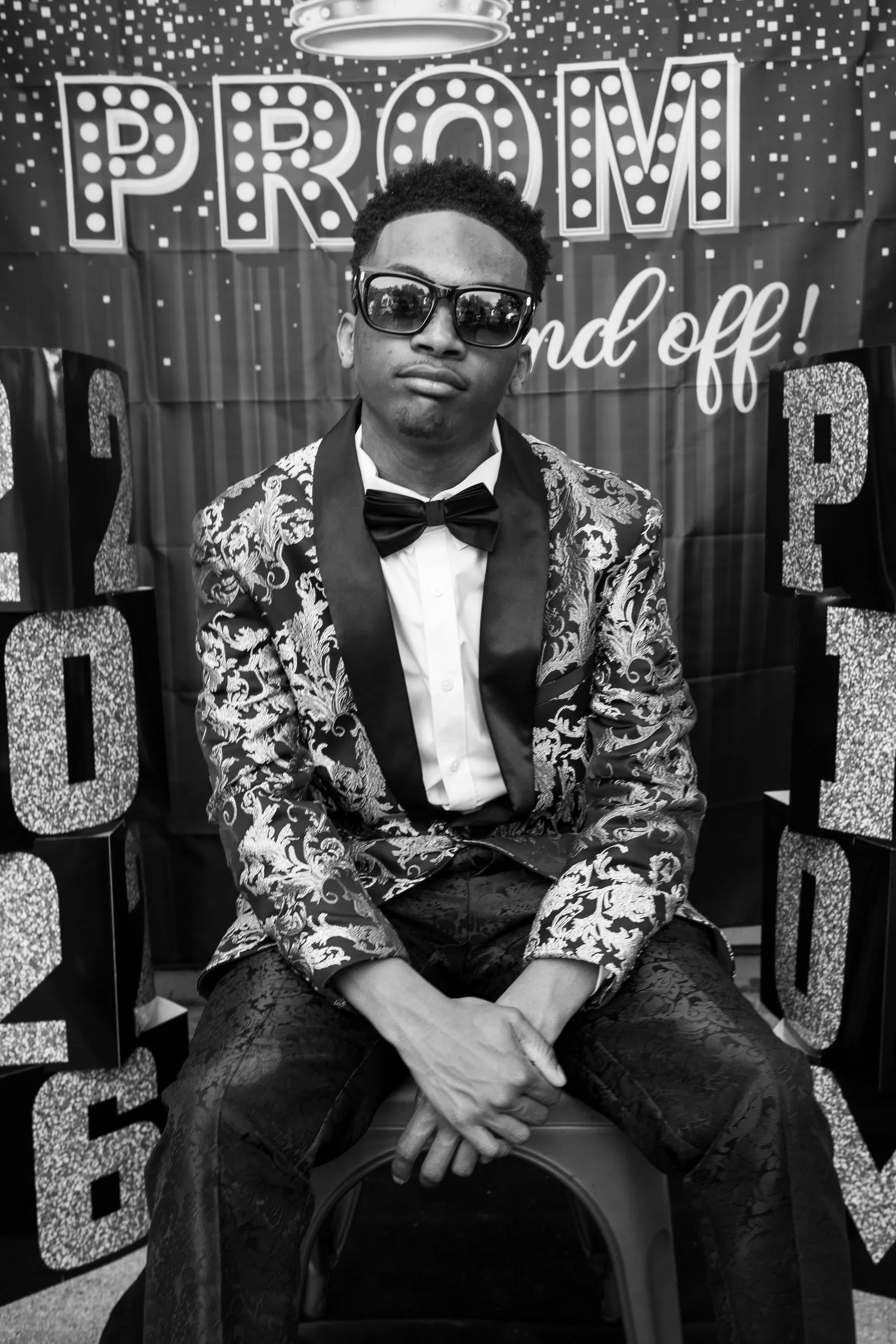Black and white seated portrait in sunglasses at the send-off backdrop