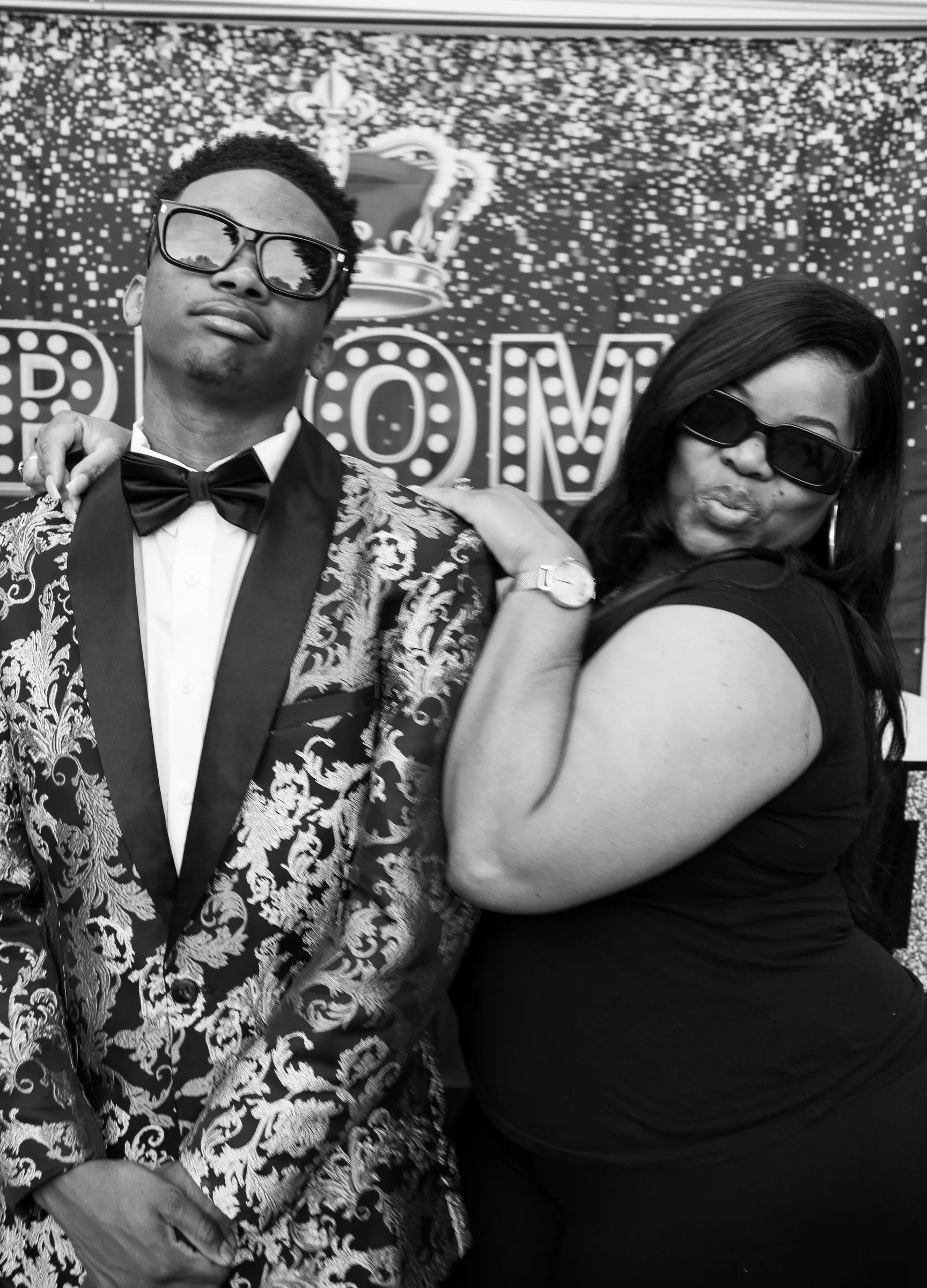Black and white photograph of him posing with a woman in sunglasses at the backdrop