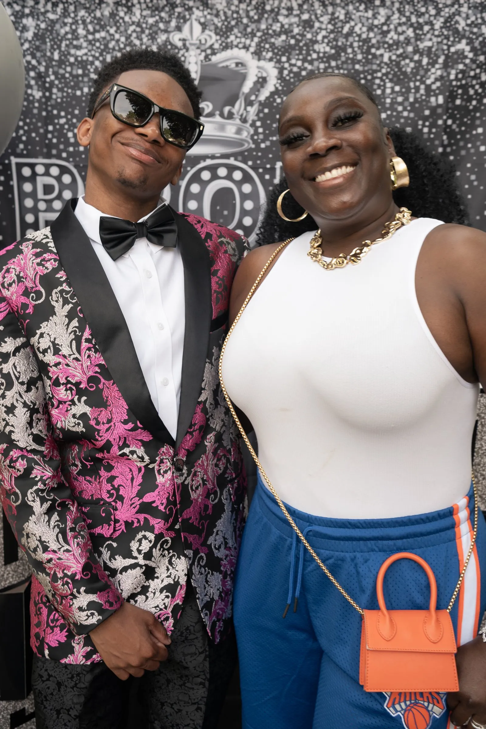 He smiles with a guest in a white top and gold necklace