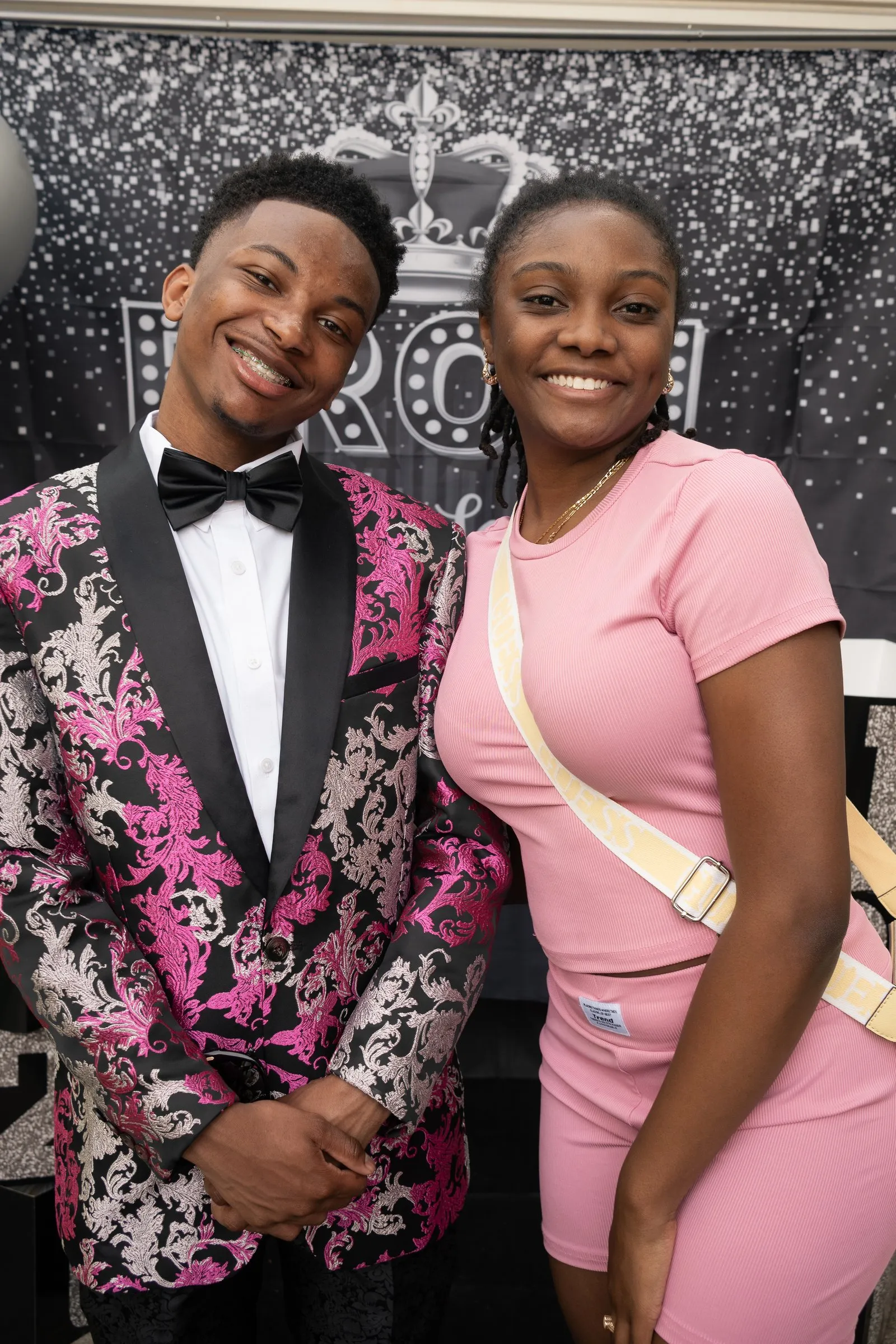 He poses with a friend in a pink outfit at the backdrop