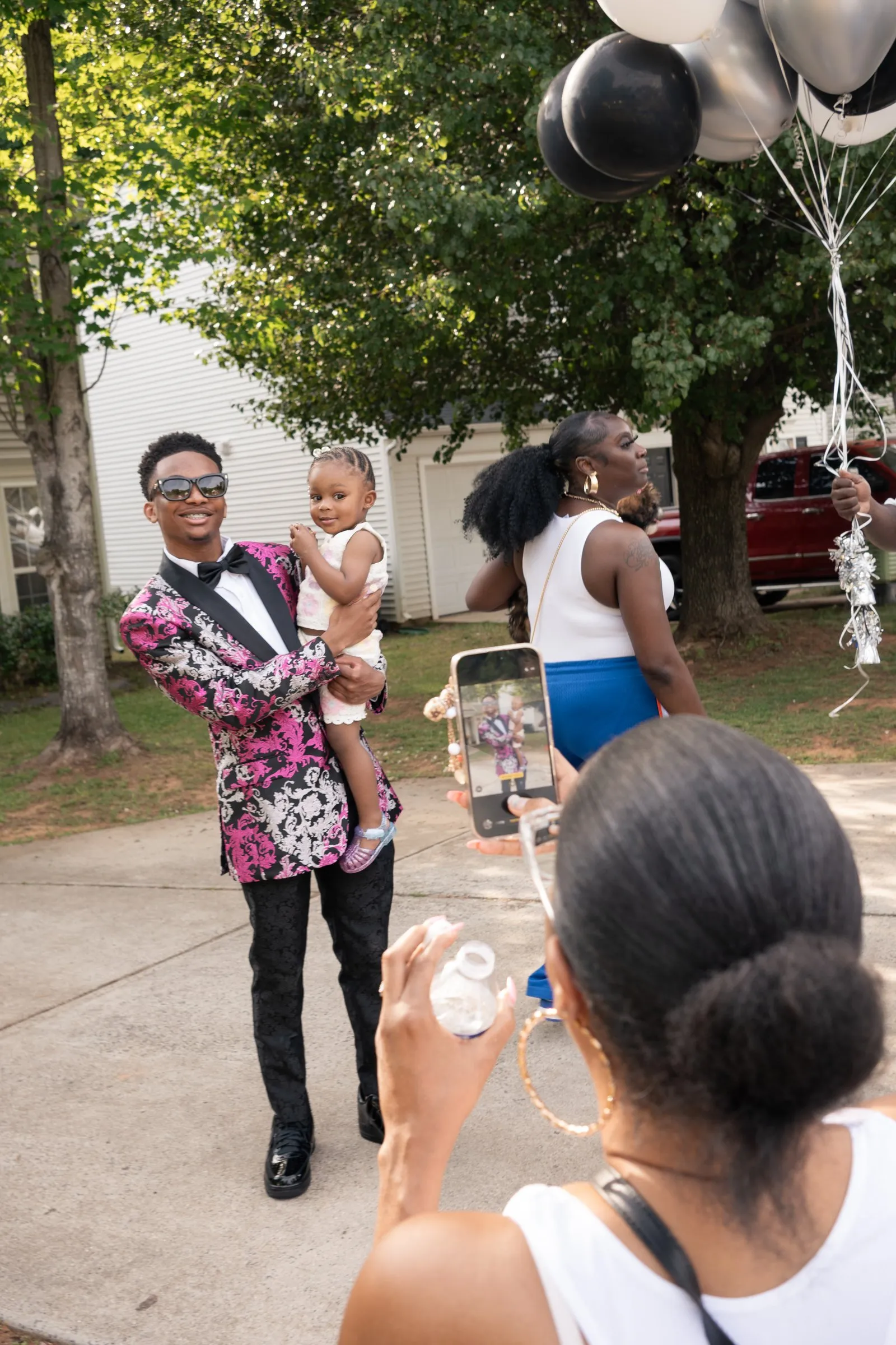 He walks down the driveway holding a toddler as guests film on their phones